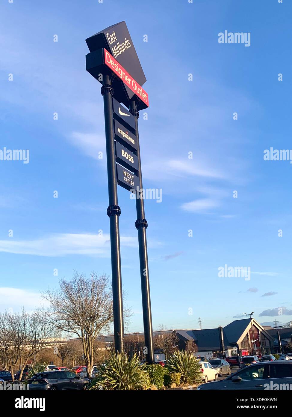 L'alto cartello dell'East Midlands designer Outlet con i loghi di Nike Boss e Levi's fotografato in una giornata limpida nel centro commerciale del Regno Unito - Immagine stock catturata con smartphone