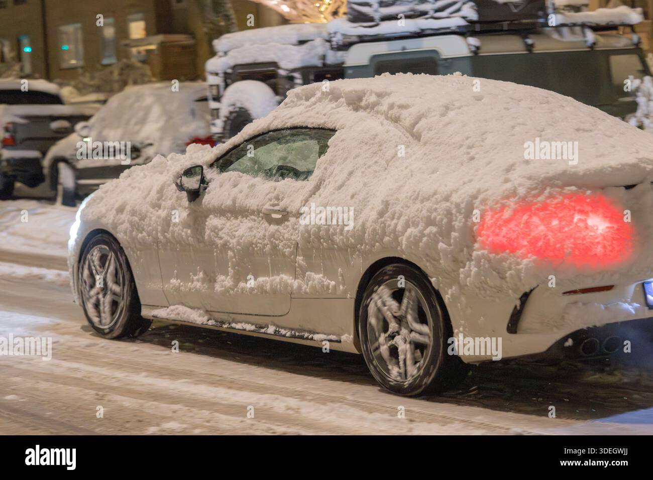 Un'auto coperta di neve con scarsa visibilità guida durante la notte Foto Stock