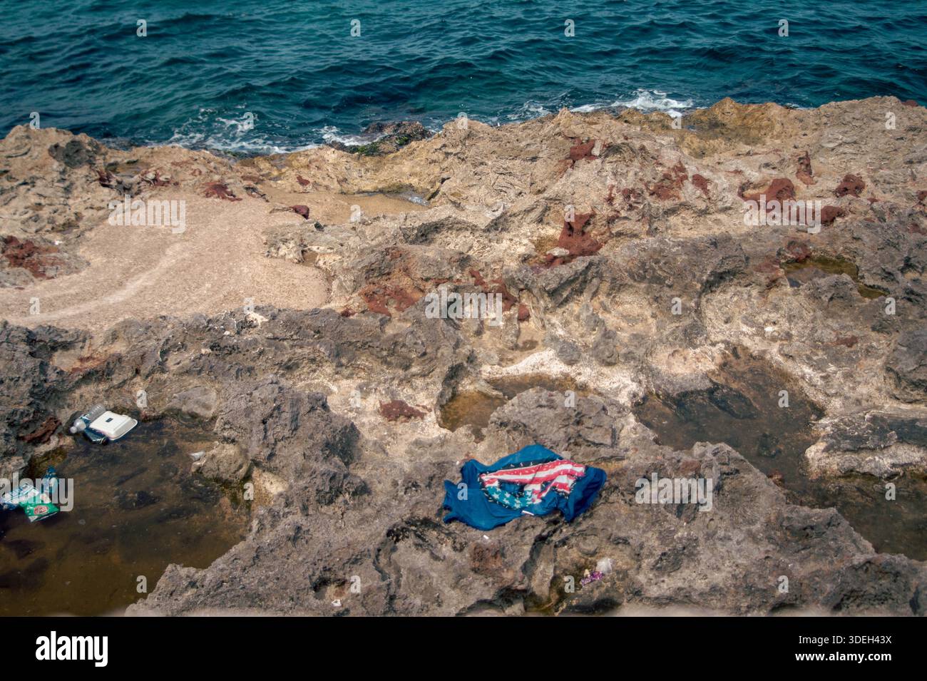 Rifiuti di plastica e vestiti scartati abbandonati su un'aspra costa rocciosa vicino all'oceano a l'Avana, Cuba. Uno sguardo fermo all'inquinamento ambientale. Foto Stock