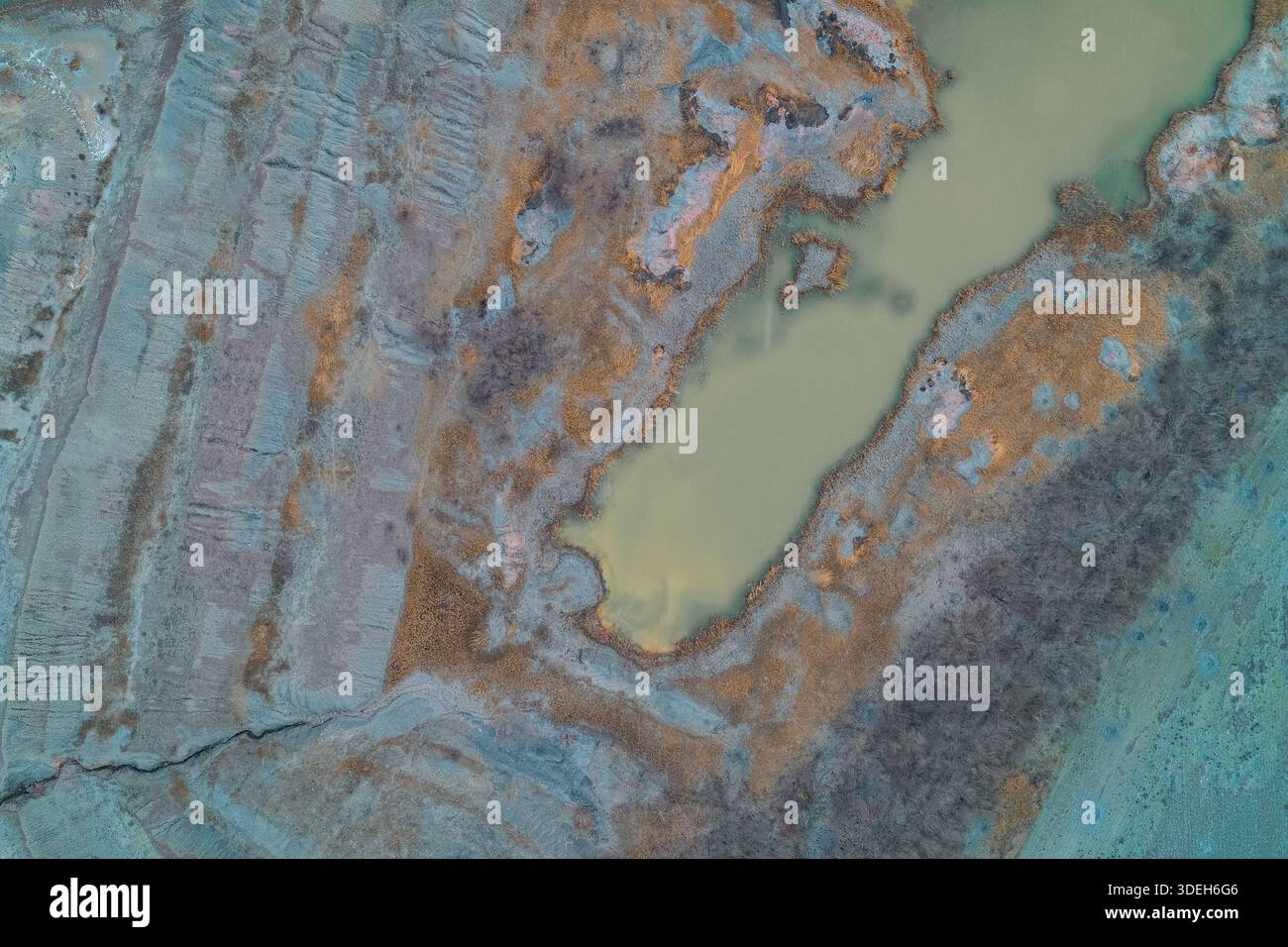 Cupa vista aerea dall'alto di una torbida piscina di acqua verde in un sito di scavo industriale. Il lago inquinato circondato da argilla grigia erosa e vegetazione secca illustra i danni ambientali e la contaminazione del suolo. Copia spazio. Foto Stock