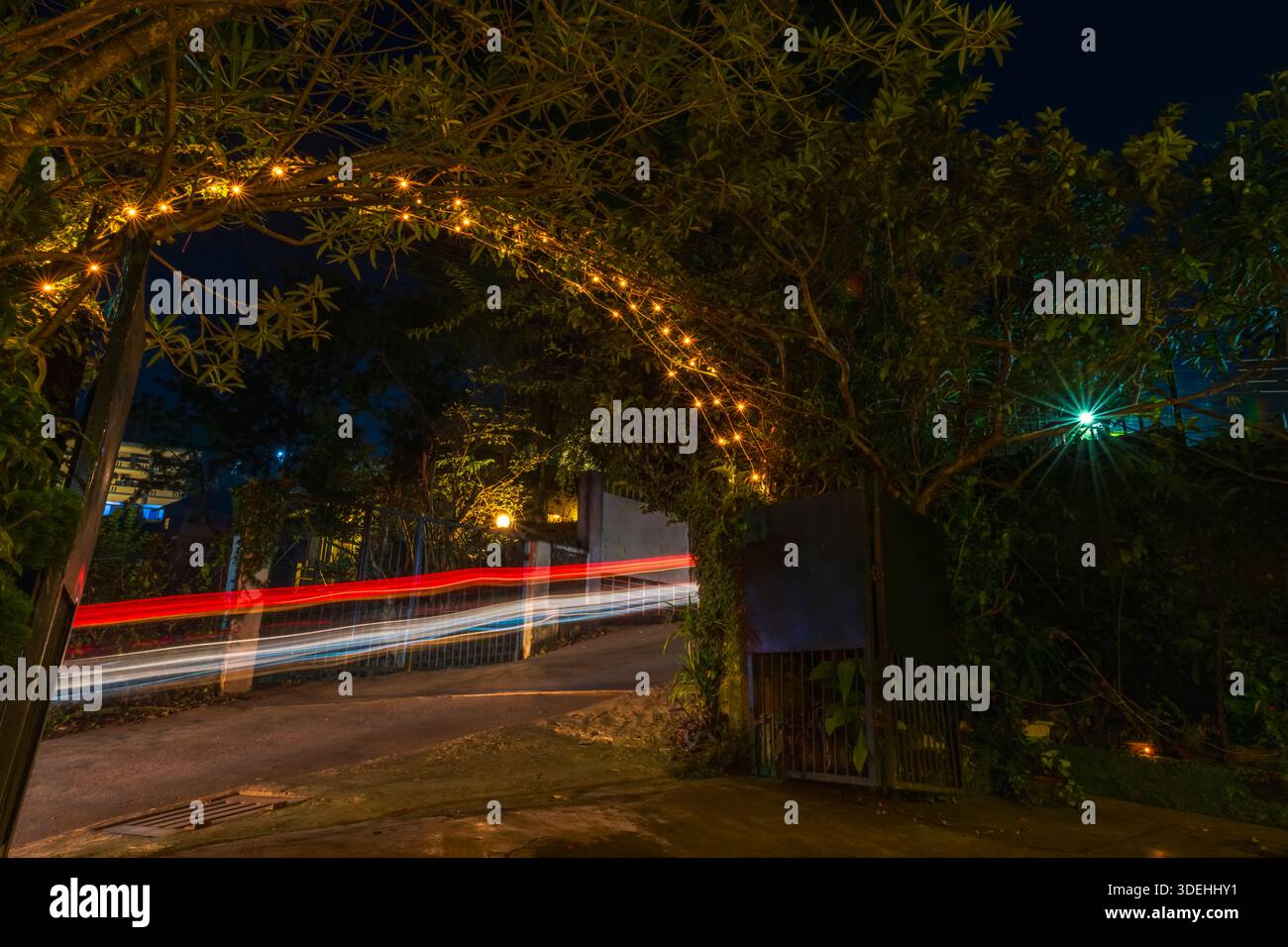 Un arco di metallo sopra un cancello di metallo decorato con luci a corda per Diwali. Nell'immagine sono visibili tracce di luce provenienti dai veicoli che piacciono sulla strada. Foto Stock