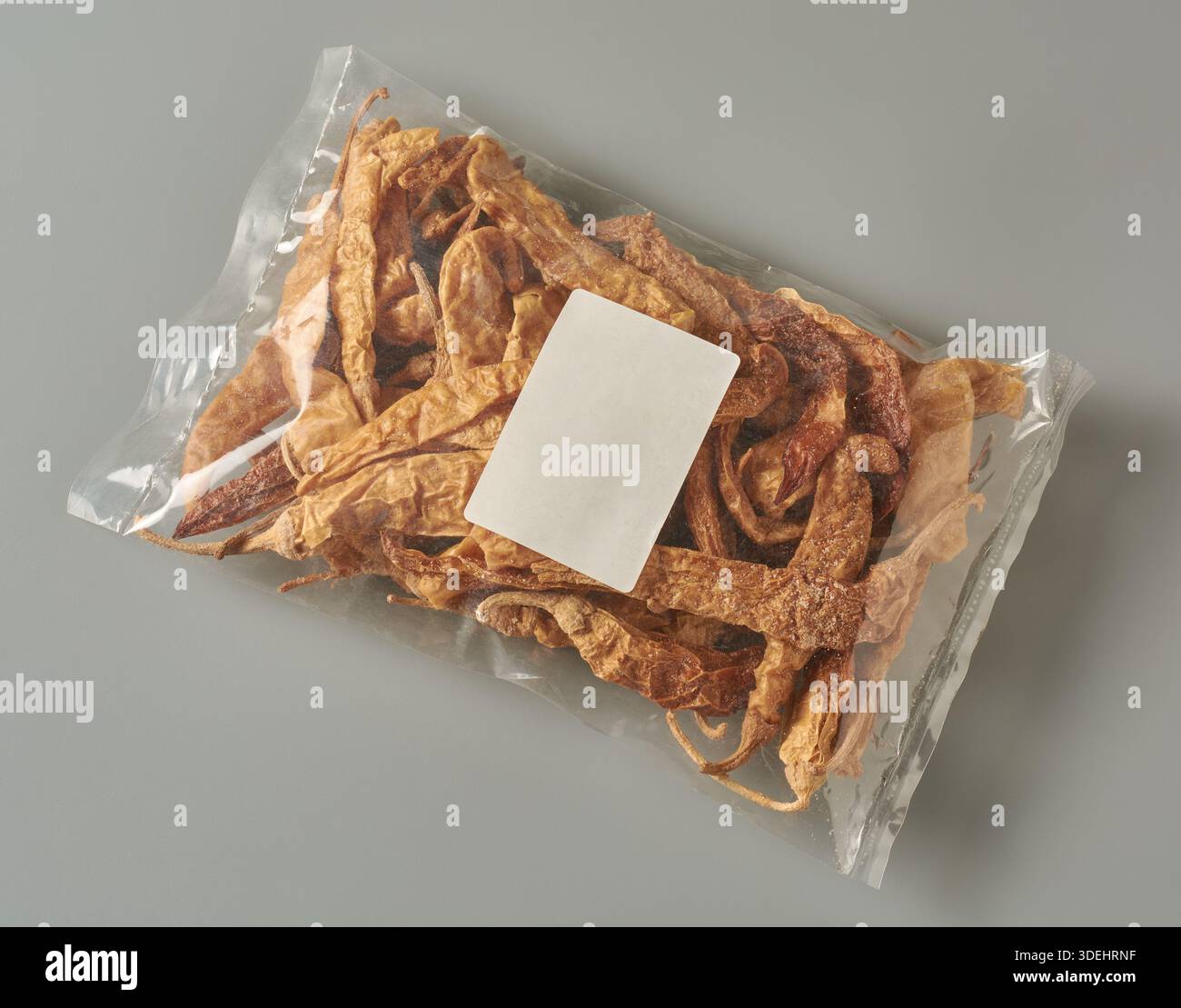 peperoncini secchi in confezione di plastica trasparente sfondo grigio neutro isolato, peperoni salati essiccati al sole visibili attraverso la confezione lucida trasparente Foto Stock