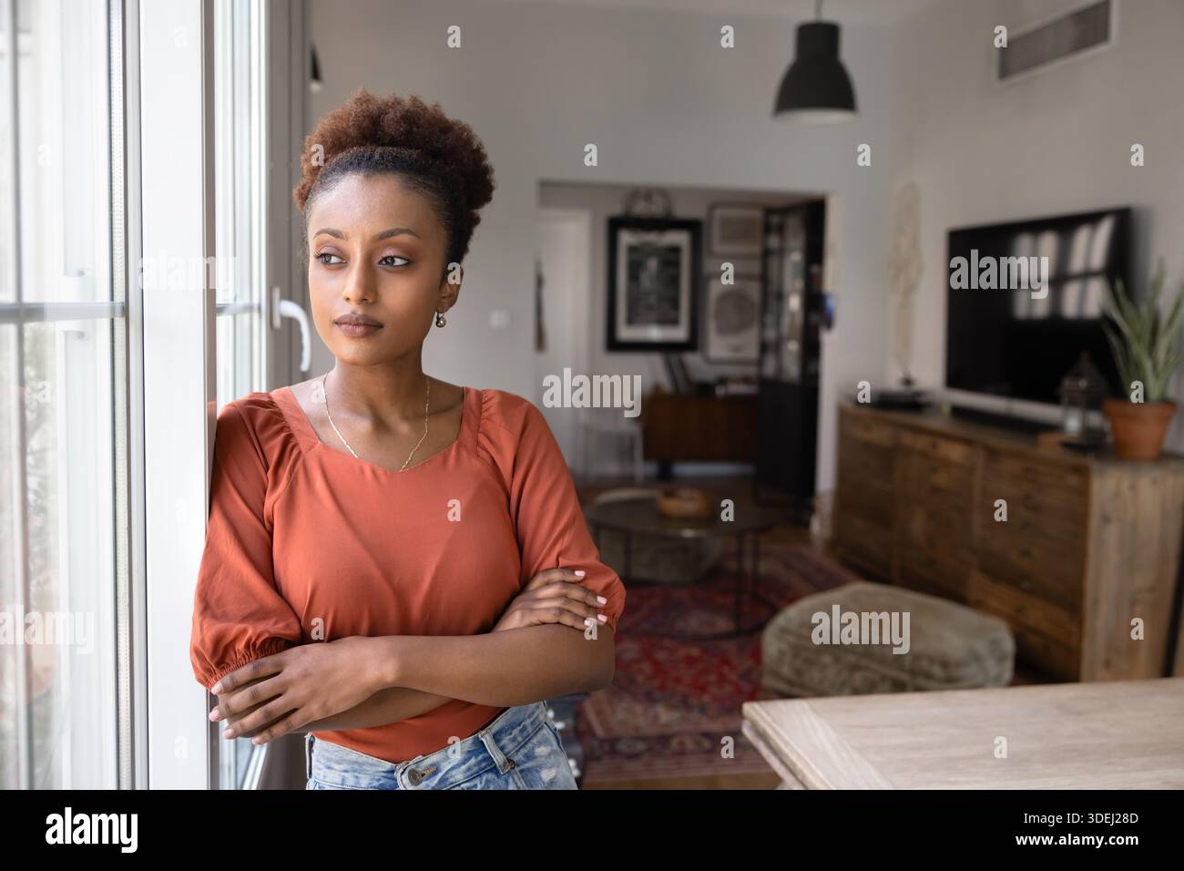 Giovane donna africana seria e premurosa in piedi alla finestra Foto Stock
