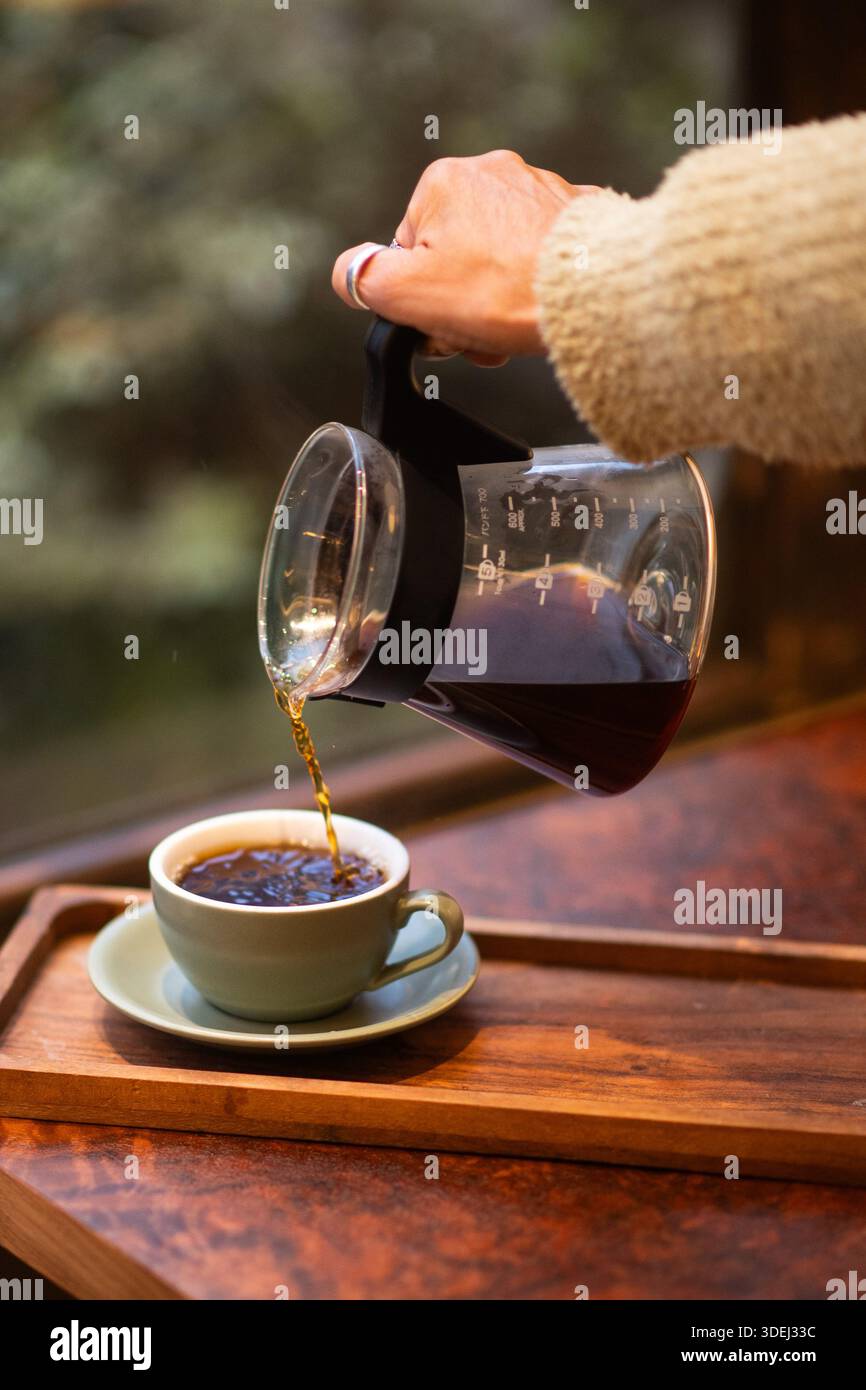 Una donna che serve caffè appena preparato in una tazza colorata in una caffetteria. Foto Stock