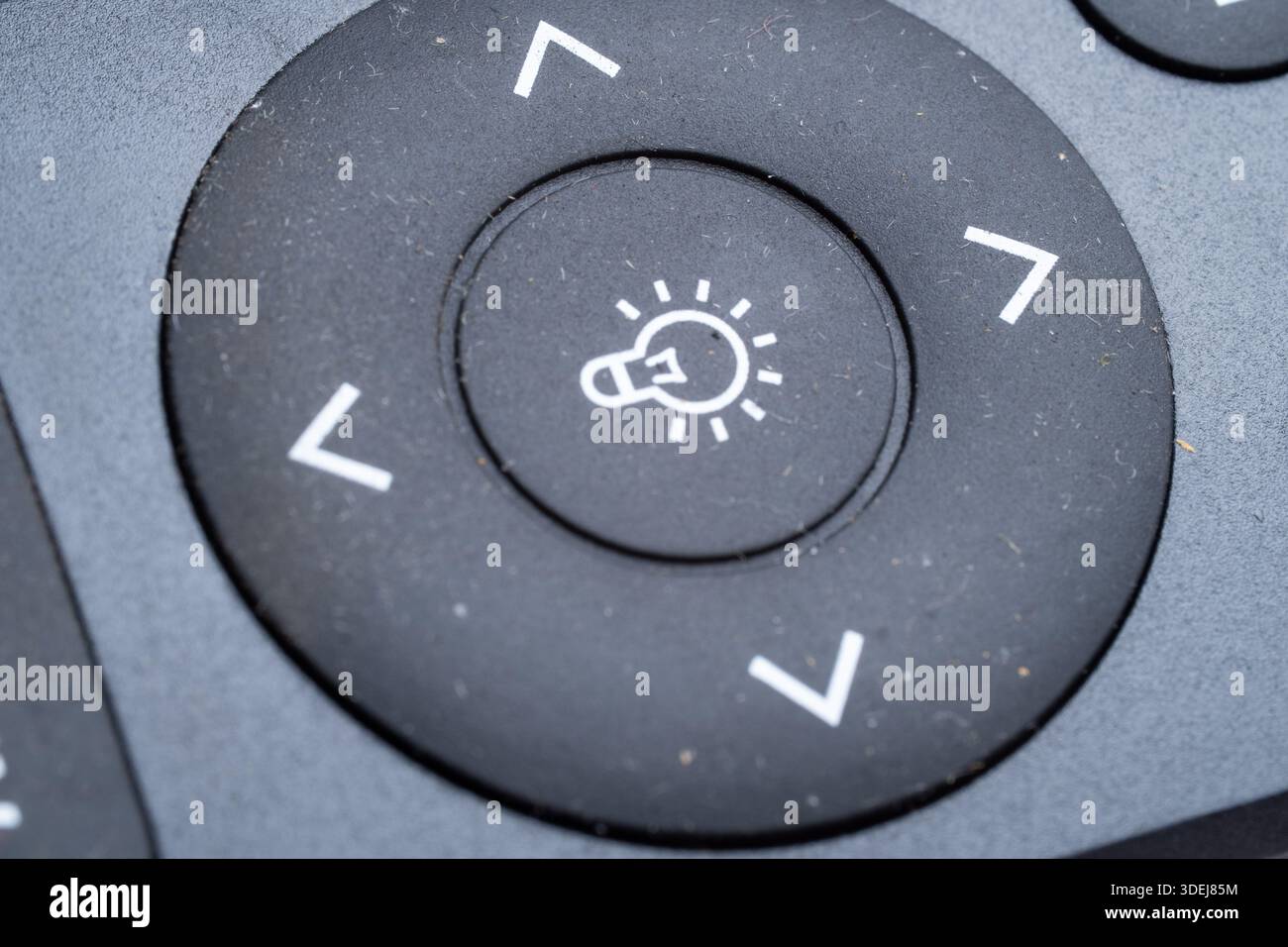 Primo piano dettagliato di un tasto del telecomando nero con un'icona di una lampadina bianca e frecce direzionali. Concetto di innovazione ed energia intelligente. Foto Stock