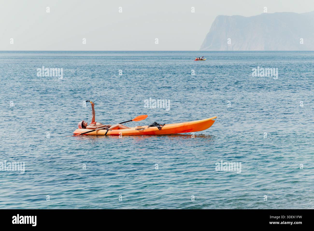 Kayak sulla costa del mare persona che si rilassa in un kayak arancione brillante su un mare calmo con una scogliera lontana sullo sfondo. Foto Stock