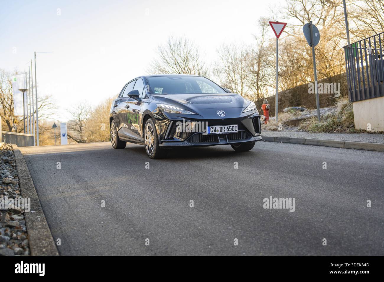 Un'auto nera ad un incrocio circondato da alberi e segnali stradali alla luce del sole, MG4 Electric car, Deer e-Carsharing, Calw, Germania Foto Stock