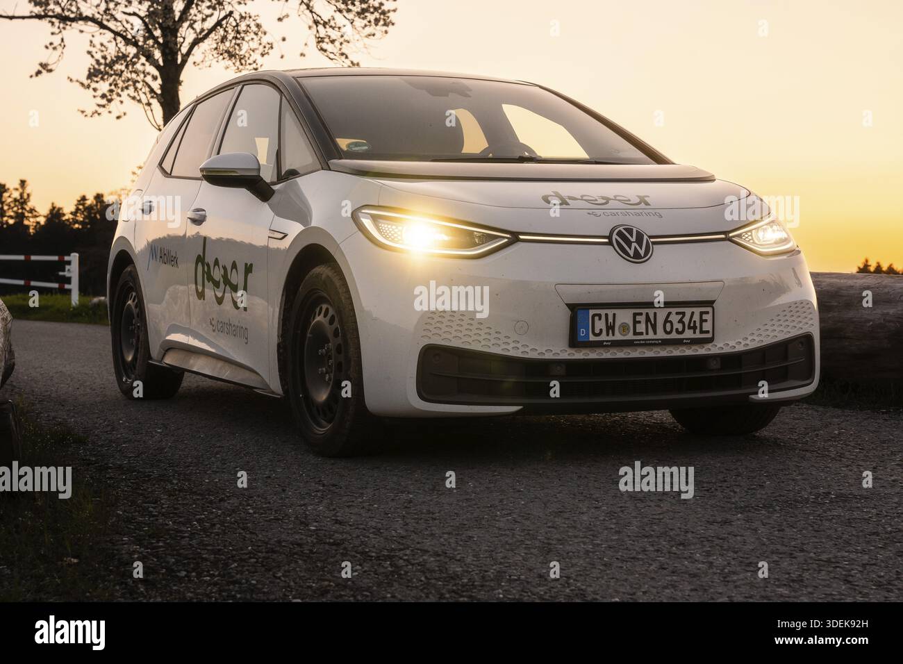 Auto su strada di campagna al crepuscolo con fari accesi, auto elettrica VW ID3, e-car sharing con cervi, Calw, Germania Foto Stock
