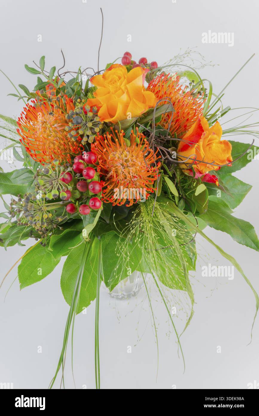 Bouquet colorato in vaso con fiori arancioni e gialli, bacche rosse e foglie verdi, protea, rose Foto Stock