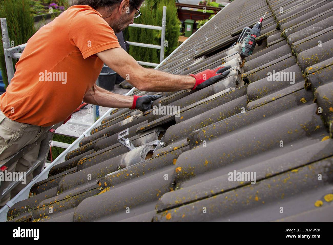 Roofer, operaio sul tetto. Lavori di copertura. Installazione cella solare. Preparazione dell'installazione di pannelli solari. fissaggio di guide, ganci. impalcatura accesa Foto Stock