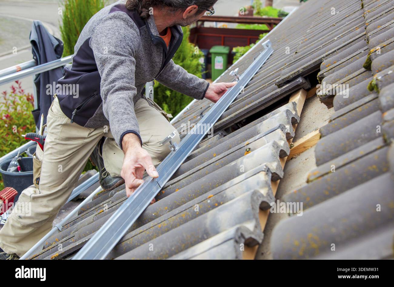 Roofer, operaio sul tetto. Lavori di copertura. Installazione cella solare. Preparazione dell'installazione di pannelli solari. fissaggio di guide, ganci. impalcatura accesa Foto Stock