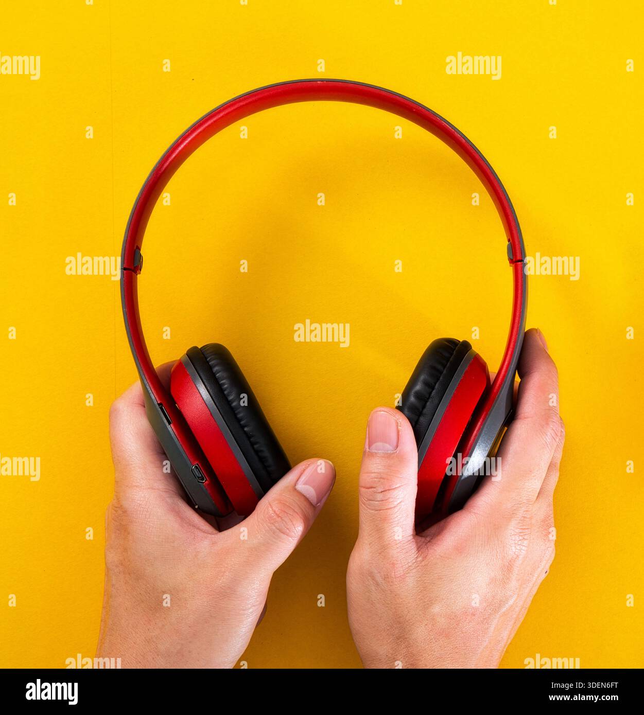 Mani che reggono le moderne cuffie wireless rosse su una superficie gialla brillante Foto Stock