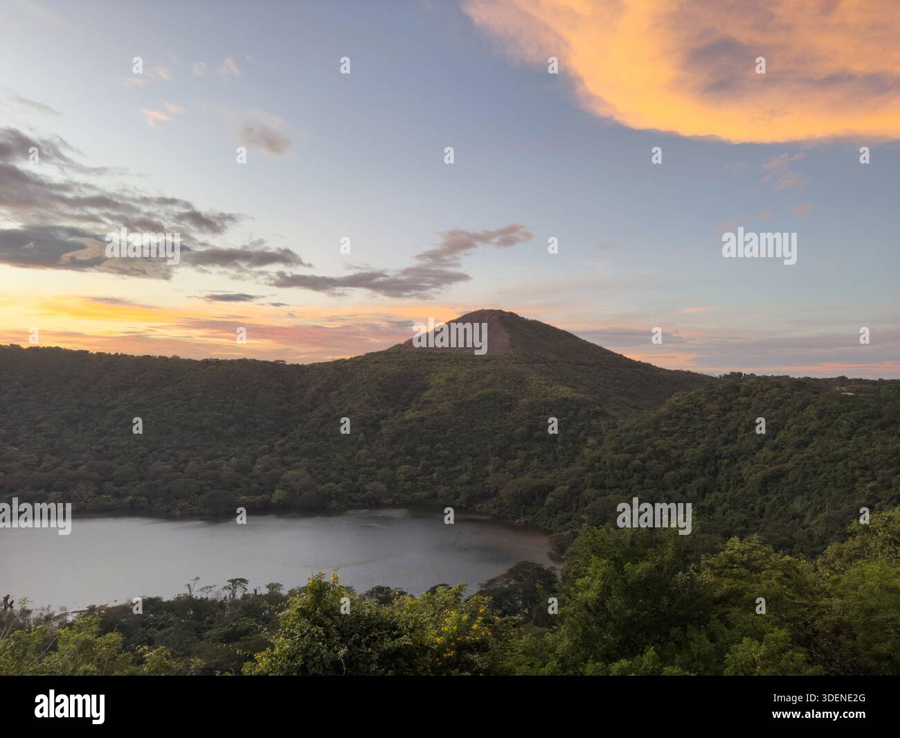Lo splendido tramonto illumina il cielo sopra il tranquillo lago vulcanico circondato da una vibrante vegetazione. Foto Stock