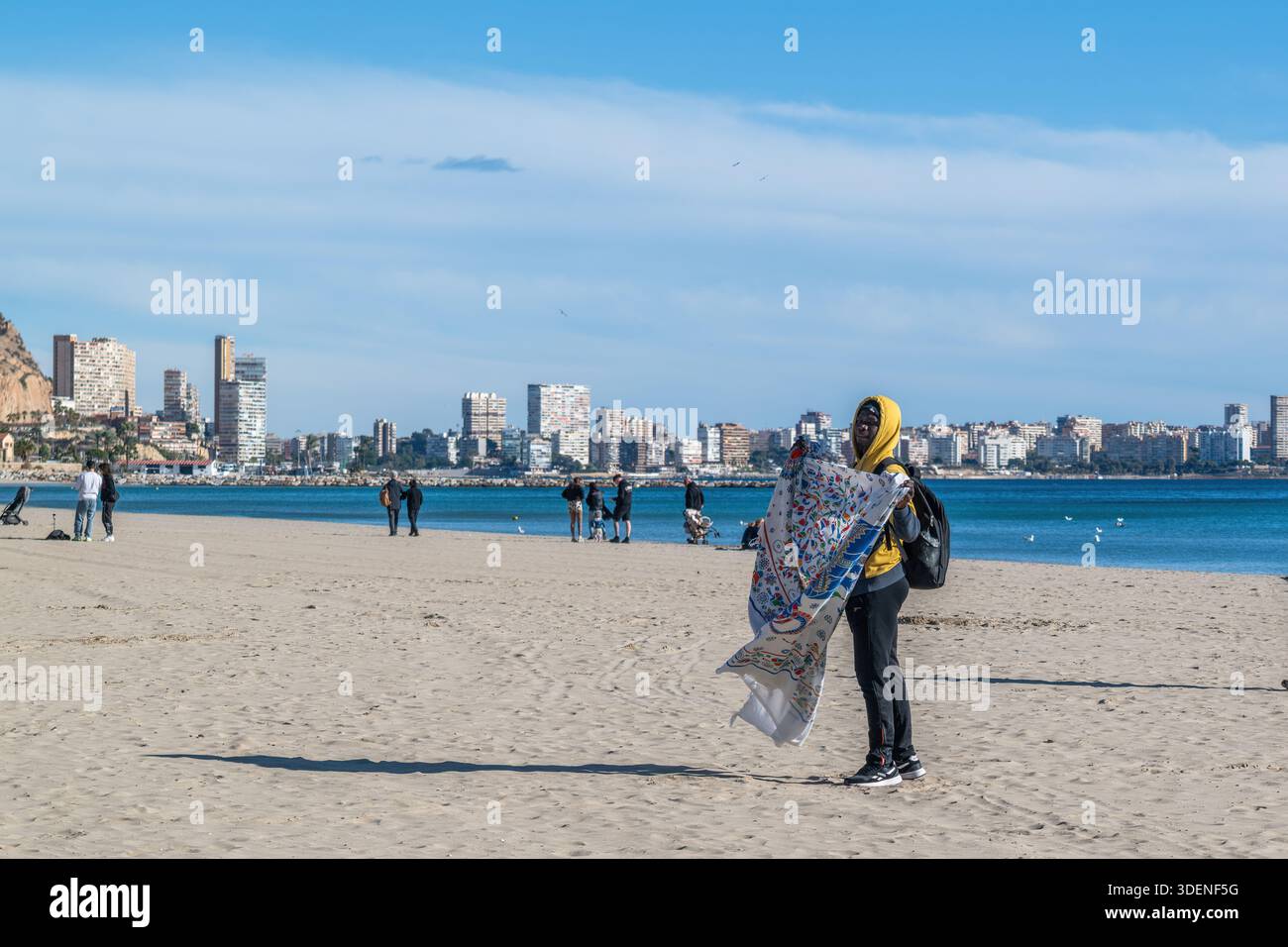 Lavoratore migrante sulla spiaggia che vende asciugamani da spiaggia ad Alicante, Spagna Foto Stock