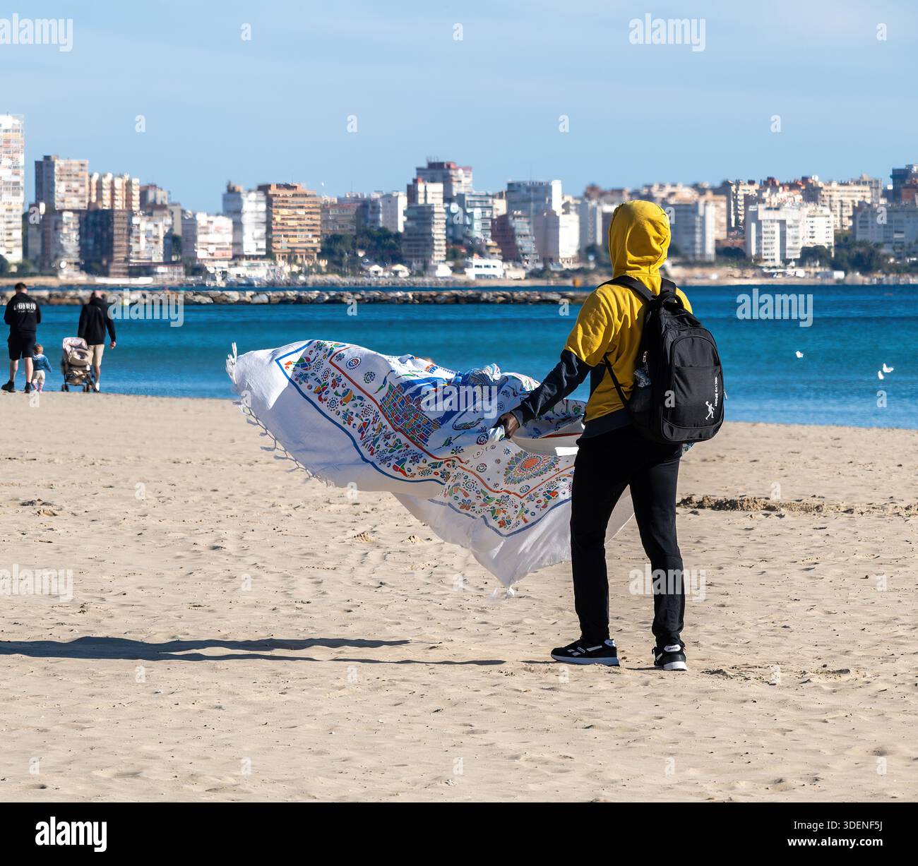 Lavoratore migrante sulla spiaggia che vende asciugamani da spiaggia ad Alicante, Spagna Foto Stock
