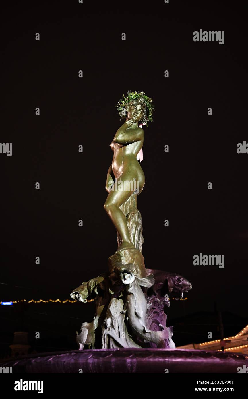 La scultura di Havis Amanda si erge illuminata contro il buio cielo invernale nel centro di Helsinki, adornata da una corona natalizia che cattura un essere Foto Stock