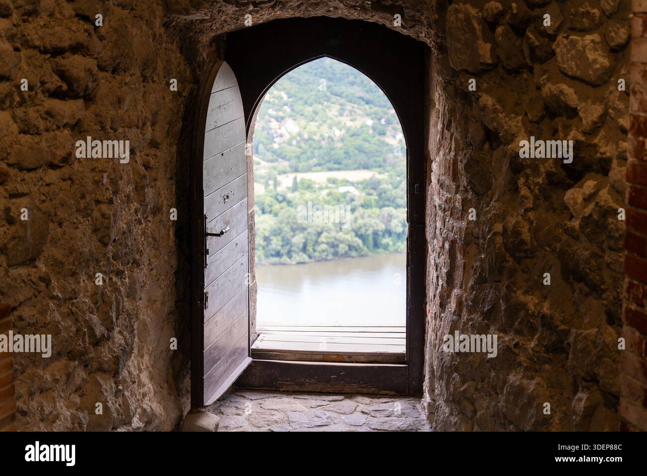 Vecchia porta di legno che si apre nel nulla in un castello storico sulla cima di una montagna, con un fiume e un paesaggio forestale in lontananza Foto Stock