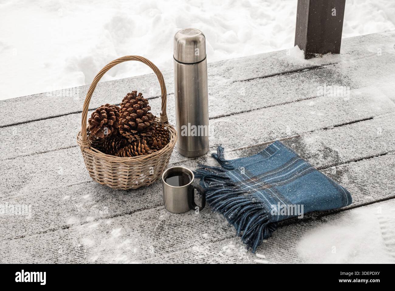 Bottiglia thermos e tazza in metallo collocate all'esterno su uno sfondo di foresta innevata. Escursioni invernali e bevande calde, ambiente naturale con clima freddo. Foto Stock