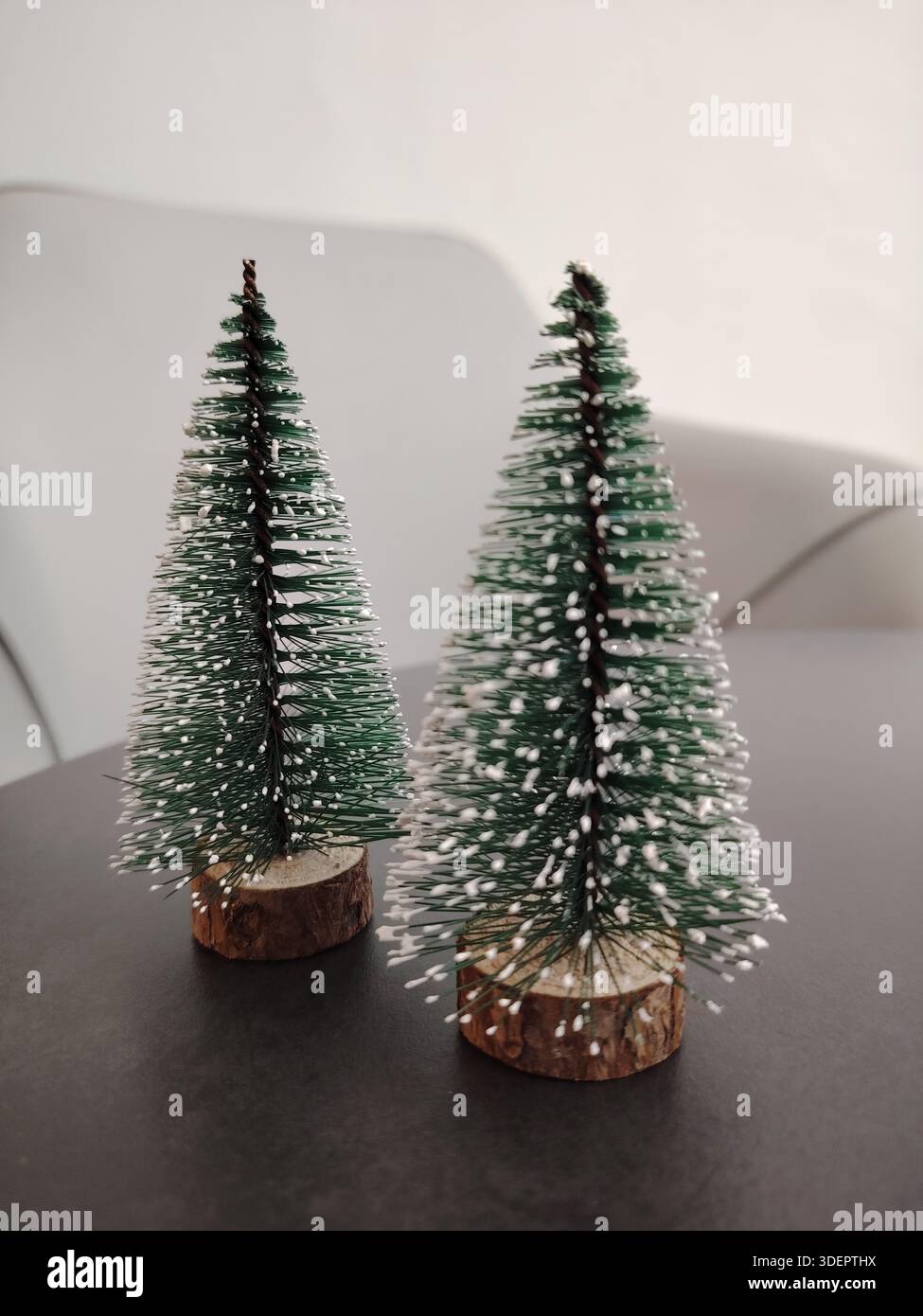 Due piccole bottiglie artificiali spazzolano gli alberi di Natale con neve finta su una superficie scura, perfette per le feste invernali. Foto Stock