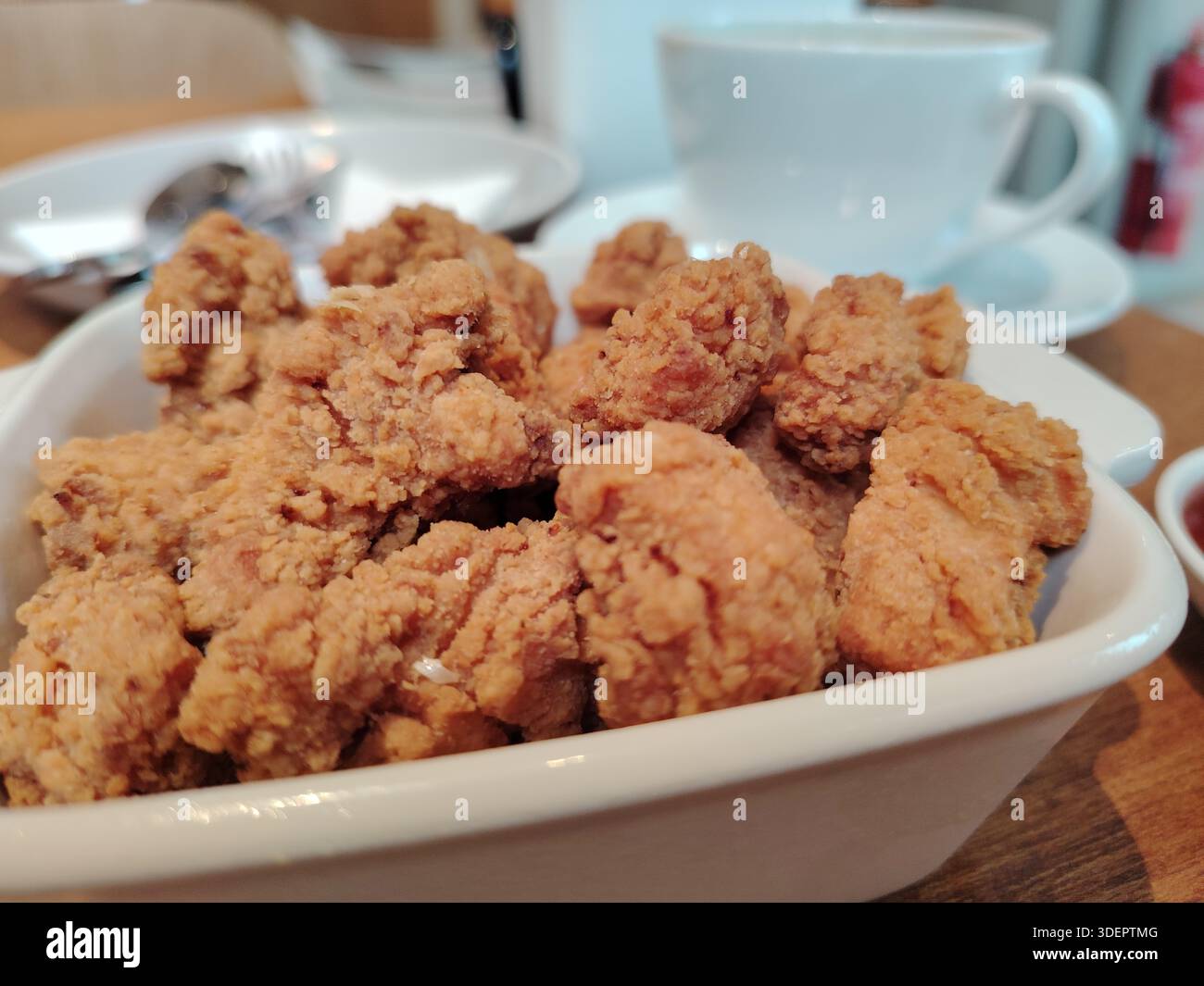 Pollo fritto croccante di popcorn in una ciotola bianca, servito su un tavolo da caffè con sfondo sfocato. Foto Stock