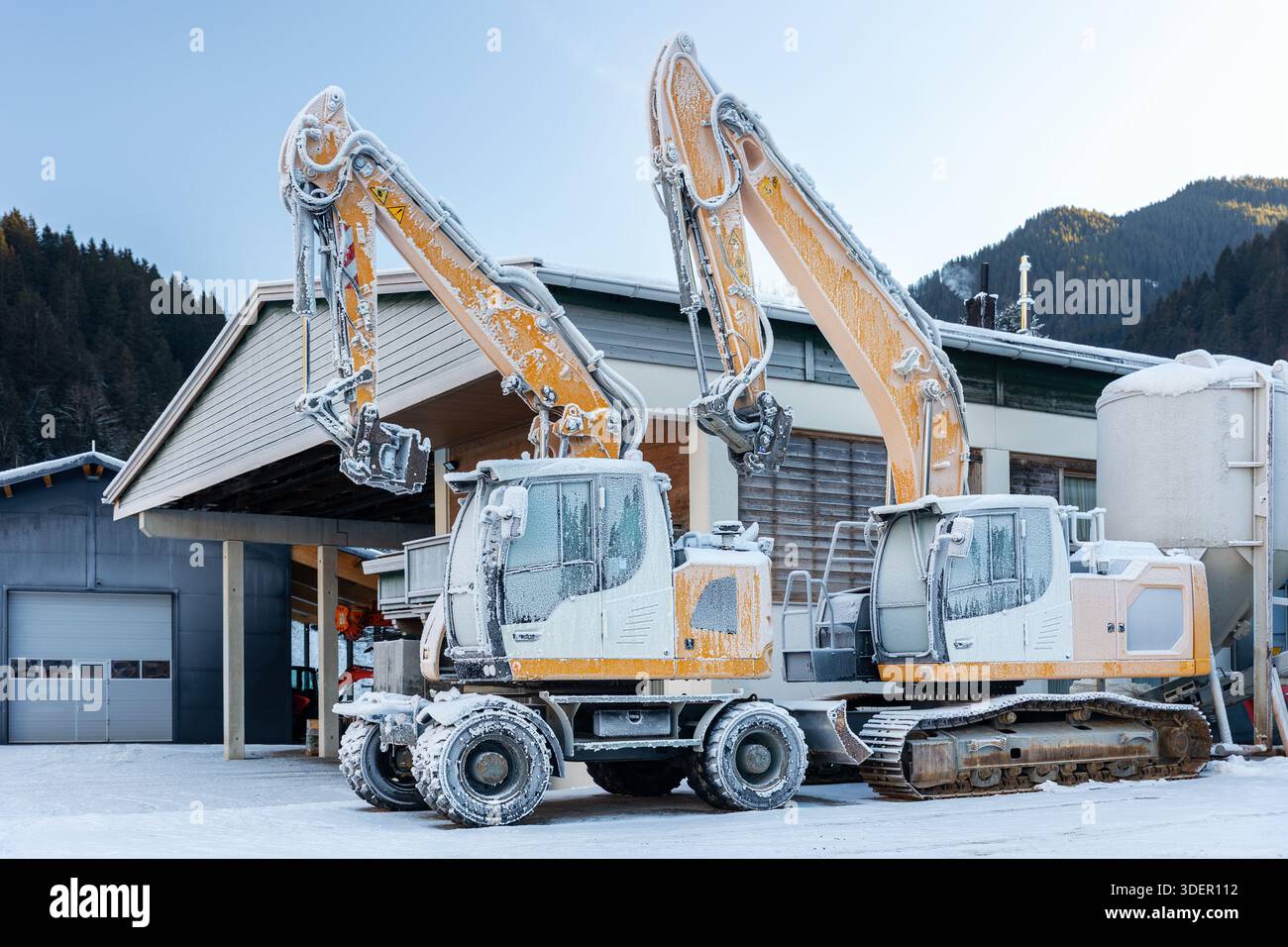 Vista panoramica escavatori idraulici congelati all'aperto condizioni invernali neve coperta ghiaccio industriale edificio alpino. Impatti a basse temperature Foto Stock