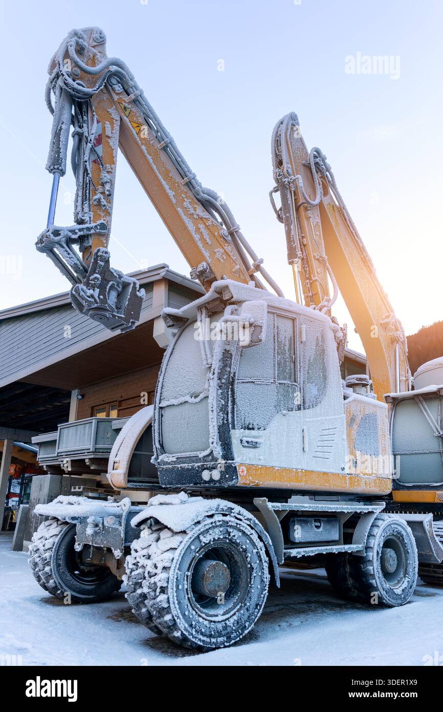 Vista panoramica escavatori idraulici congelati all'aperto condizioni invernali neve coperta ghiaccio industriale edificio alpino. Impatti a basse temperature Foto Stock