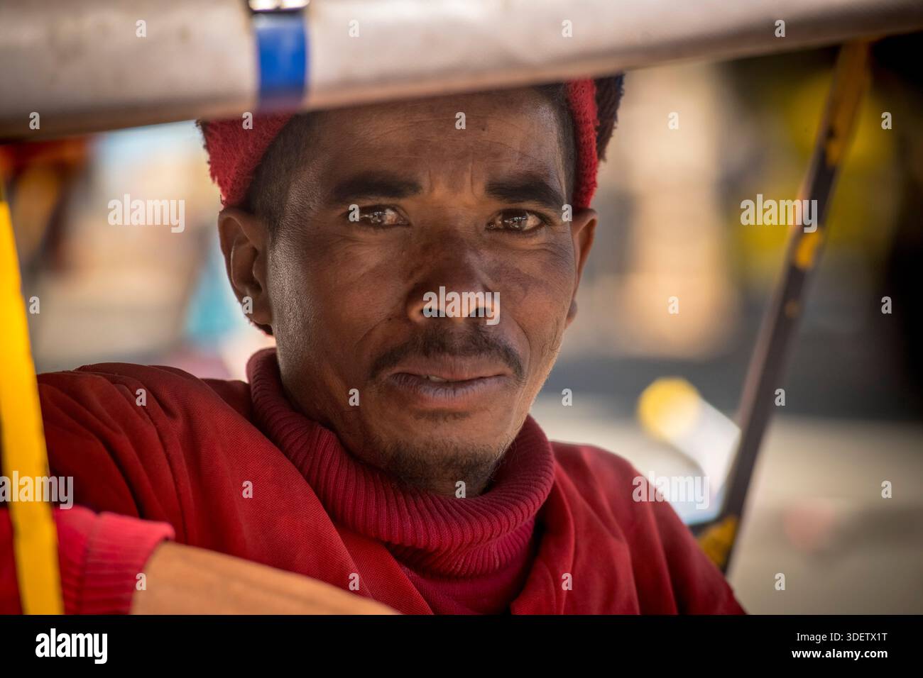 Un ritratto di un operoso autista di pousse-pousse ad Antsirabe, la "capitale del risciò" del Madagascar. Questi risciò a ciclo sono un mezzo di trasporto locale primario. L'autista, un membro della comunità locale, è uno spettacolo comune in questa vivace città, navigando per le strade per il suo sostentamento. Antsirabe, Madagascar. Foto Stock