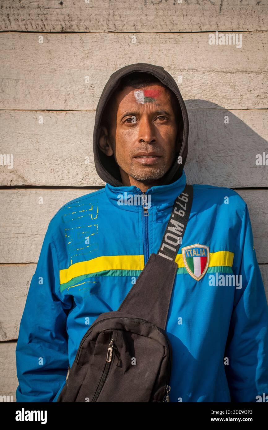 Ritratto di un malgascio in piedi contro una parete bianca con una giacca con il distintivo "Italia", mentre al tempo stesso sfoggia gli stessi colori dipinti sulla fronte - rosso, verde e bianco - secondo la bandiera nazionale malgascia. Quest'uomo aveva passato la notte a guardare la sua squadra nazionale giocare nella finale di una finale di calcio internazionale (la sua squadra ha perso). Ambositra, Madagascar. Foto Stock
