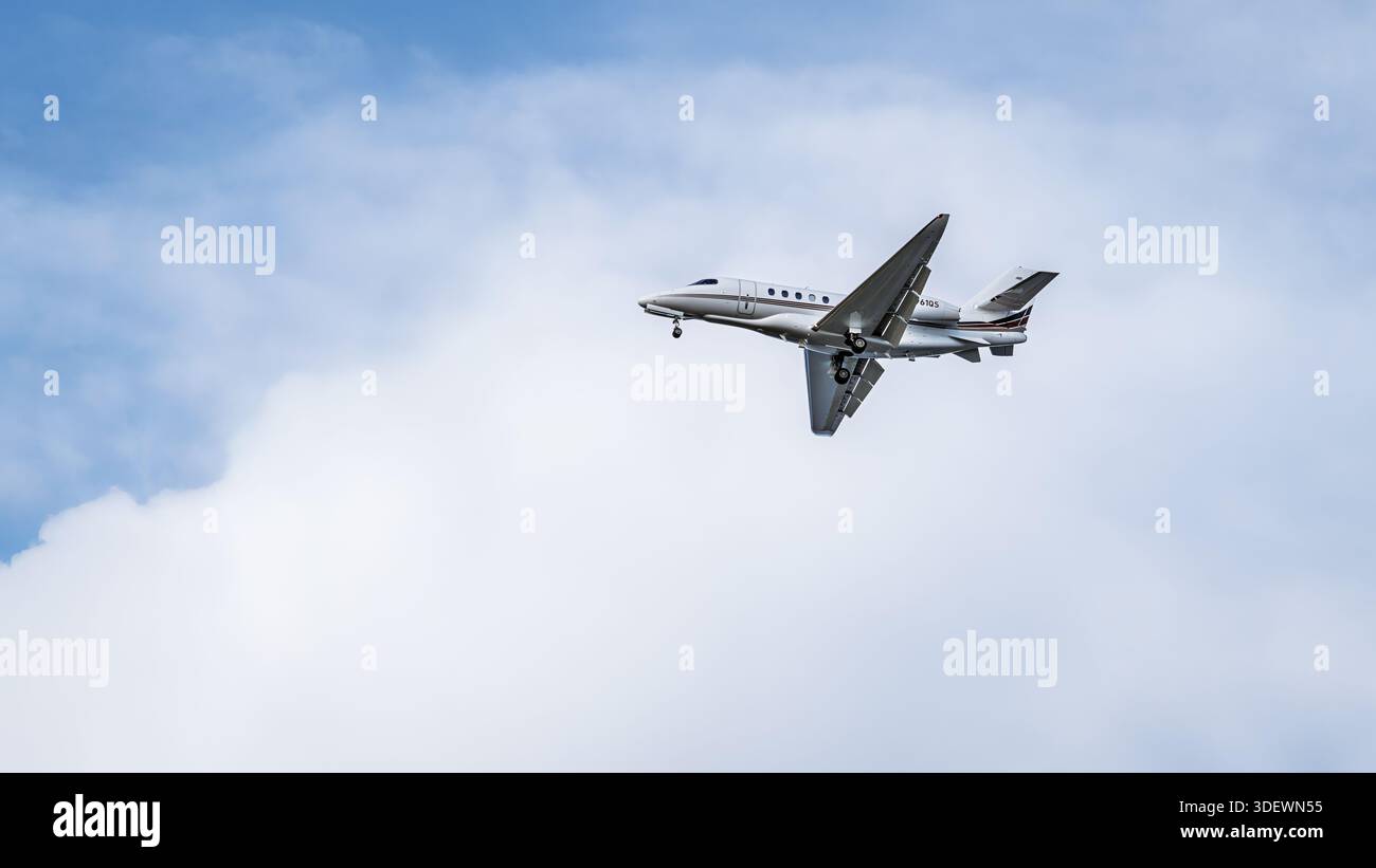Un business jet Cessna Citation Latitude vola contro un cielo nuvoloso, catturato in bianco e nero. Foto Stock