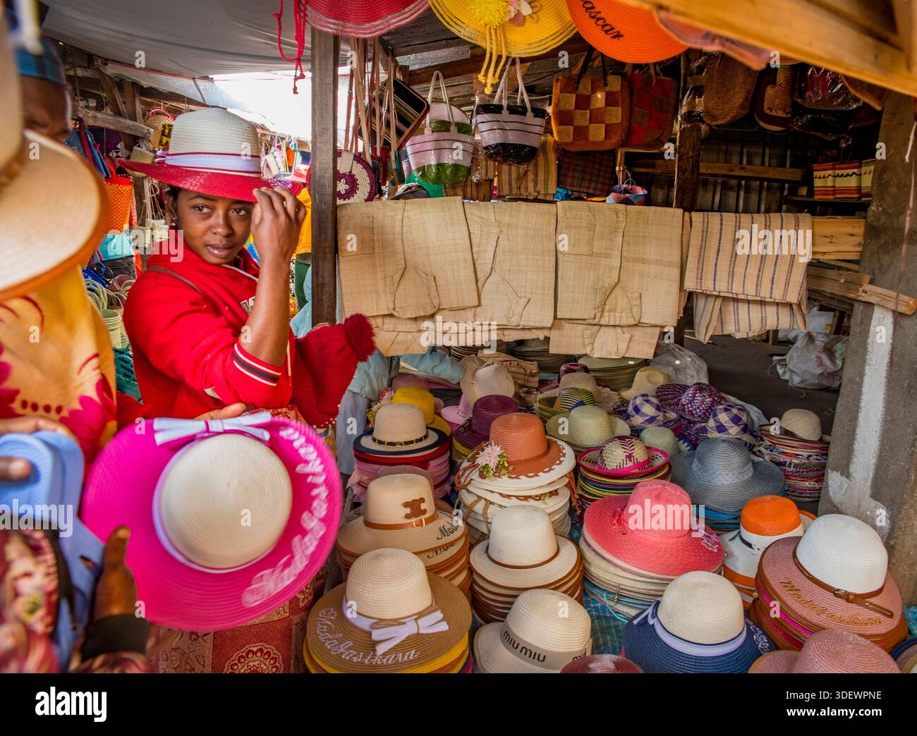 Donna malgascia che prova i cappelli al mercato Fianarantsoa. Questi cappelli di fabbricazione malgascia, noti per la loro abilità artigianale e la funzione essenziale di fornire protezione solare, sono una vista comune e culturalmente significativa negli altopiani. Fianarantsoa, Madagascar. Foto Stock