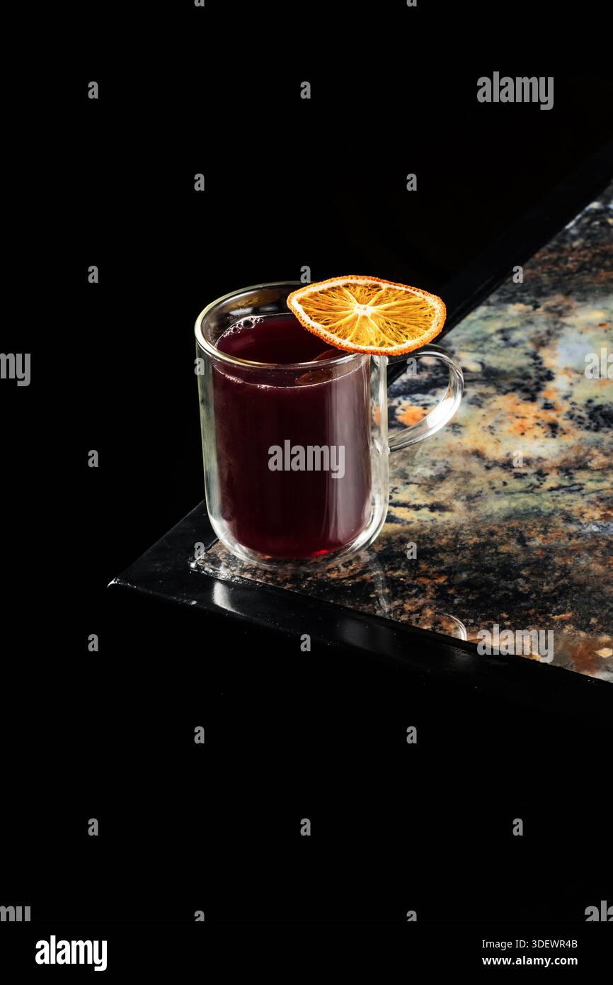 Primo piano caldo e invitante di un bicchiere di vino rosso brulé con spezie e fette di arancio, che mostrano colori ricchi e texture festose, perfetto per la festa Foto Stock