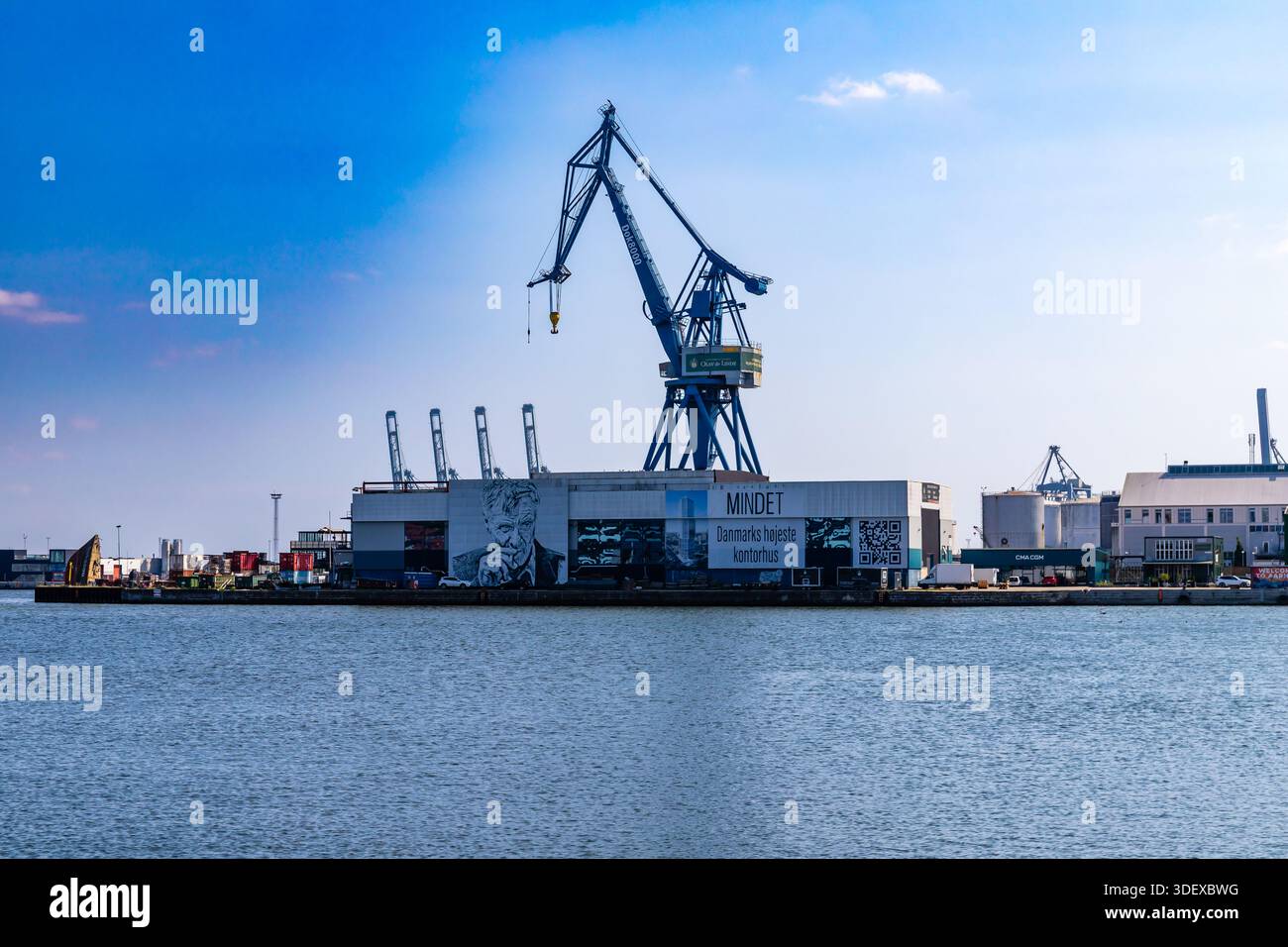 Aarhus, Danimarca - 15 agosto 2025: Edificio Mindet con grande murale e testo, dominato da torreggianti gru industriali blu contrassegnate dalla linea Ottan ad Aarhus Foto Stock
