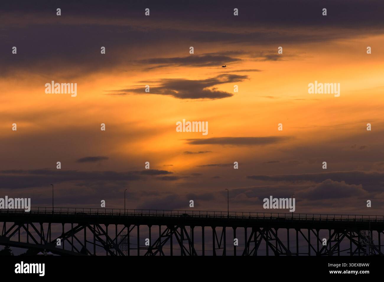 Il ponte sagomato attraversa l'orizzonte sotto un suggestivo cielo al tramonto, con nuvole luminose e luce che svanisce creando un'atmosfera serena e cinematografica Foto Stock