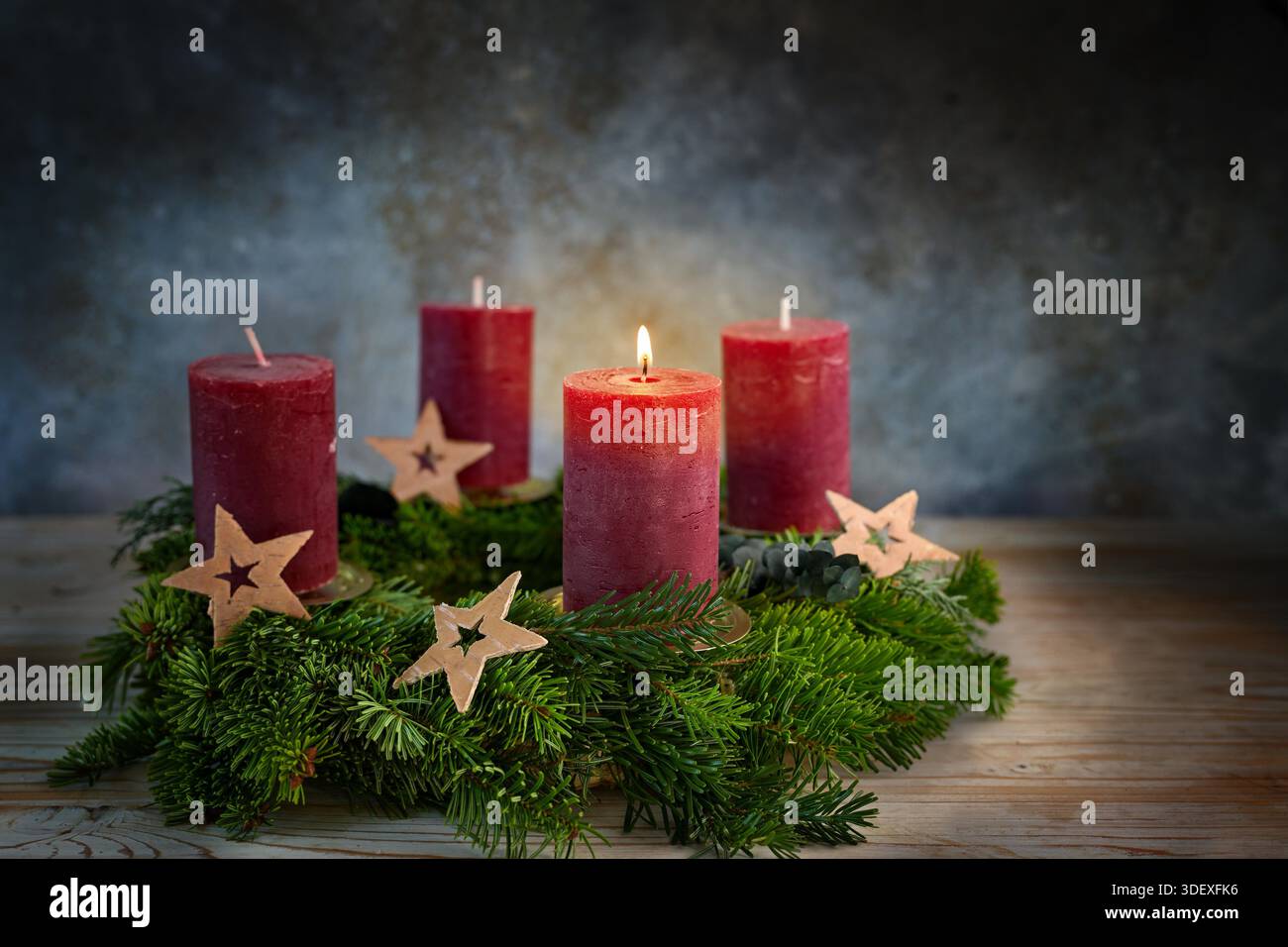 Quattro candele rosse su una corona dell'Avvento, una accesa per il primo avvento, piccole stelle come decorazione natalizia, sfondo blu scuro, spazio copia, messa a fuoco selezionata, profondità di campo ridotta Foto Stock
