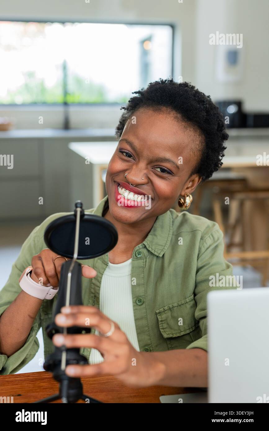 Donna afroamericana sulla trentina che fa podcasting in cucina usando il microfono con filtro pop Foto Stock