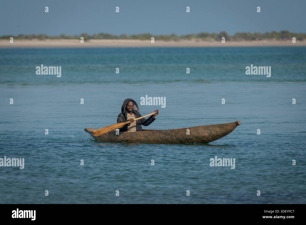 Un malgascio guida con competenza la sua canoa (pirogue) attraverso le acque poco profonde e blu appena al largo del Canale del Mozambico, vicino a Belo Sur Mer, Madagascar occidentale. Probabilmente è un pescatore di Vezo, una comunità il cui nome letteralmente significa "gente che pagaia" e che si affida pesantemente a queste tradizionali barche di legno per il loro sostentamento. La scena, con la vasta distesa dell'Oceano Indiano sullo sfondo, cattura il ritmo semplice, ma vitale, quotidiano della vita costiera e dei tradizionali metodi di pesca che hanno sostenuto il popolo Vezo per generazioni. Foto Stock