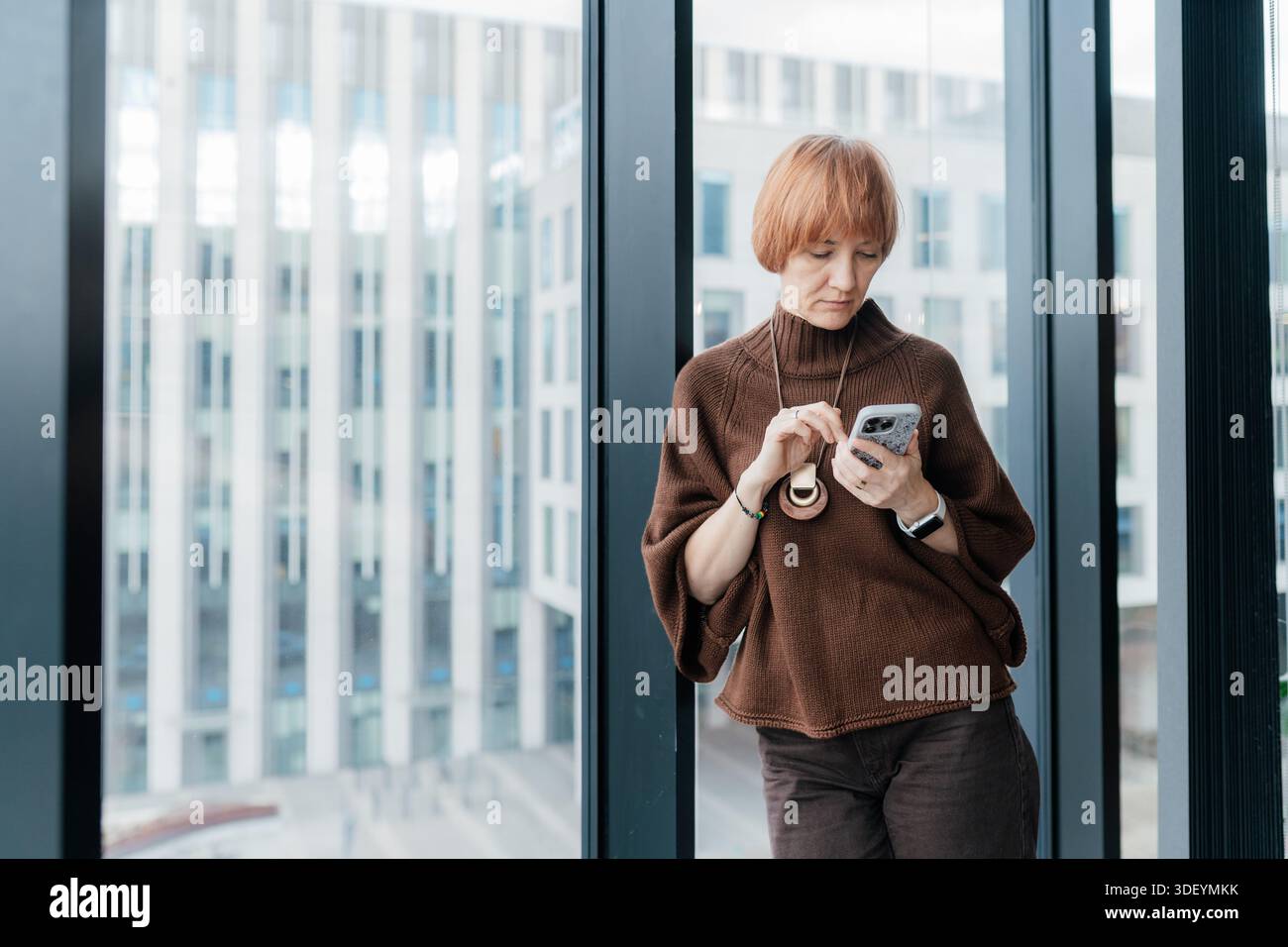 Consulente donna che controlla i messaggi telefonici nello spazio di lavoro contemporaneo Foto Stock