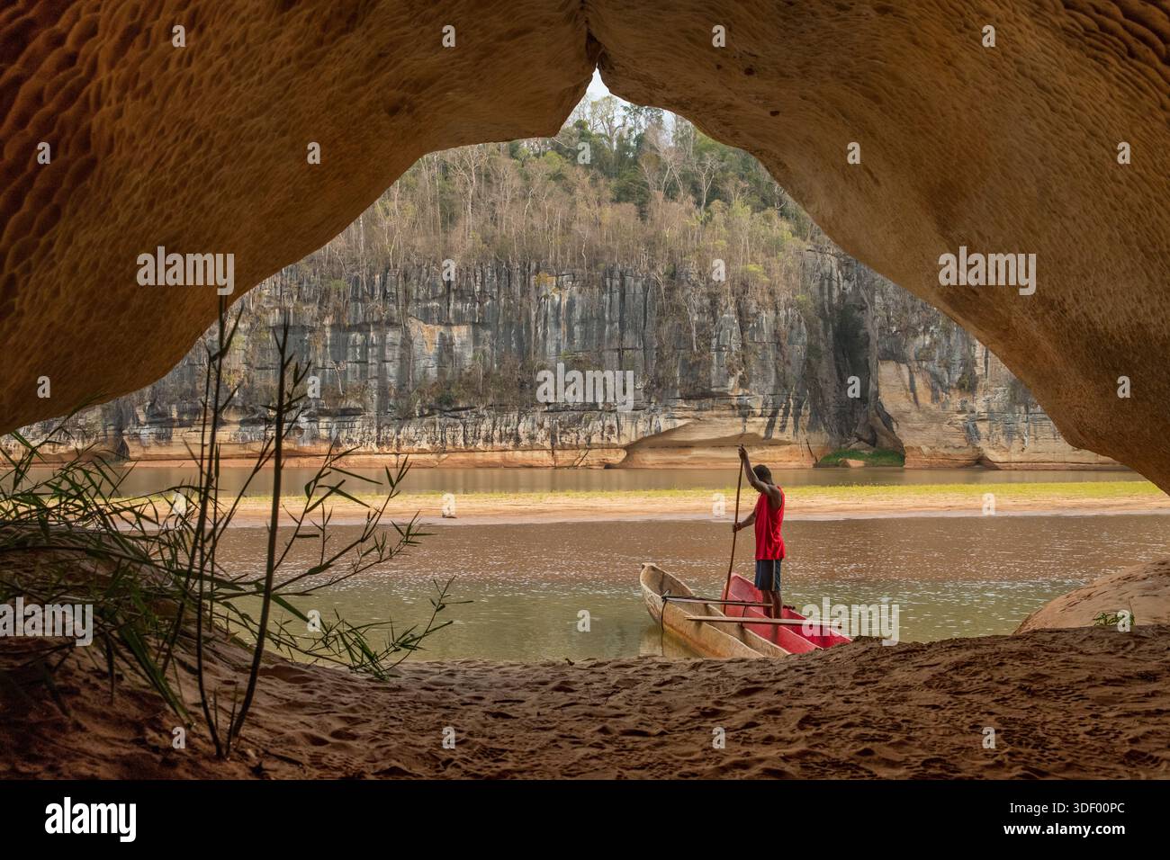 Uomo malgascio con la sua canoa all'ingresso di una grotta sulle rive del fiume Manambolo vicino a Bekopaka, Madagascar. L'area possiede un importante patrimonio culturale, poiché le scogliere e le grotte fungevano da terreno di sepoltura e siti spirituali per i Vazimba, i primi abitanti dell'isola, e per il popolo Sakalava. Una gita in canoa lungo il fiume consente ai visitatori di vedere queste tombe a scogliera e sperimentare le tradizioni locali e la storia della gente che vive lungo le rive del fiume. Foto Stock