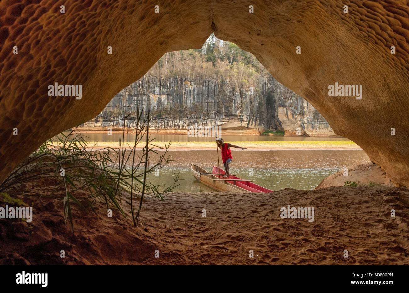 Uomo malgascio con la sua canoa all'ingresso di una grotta sulle rive del fiume Manambolo vicino a Bekopaka, Madagascar. L'area possiede un importante patrimonio culturale, poiché le scogliere e le grotte fungevano da terreno di sepoltura e siti spirituali per i Vazimba, i primi abitanti dell'isola, e per il popolo Sakalava. Una gita in canoa lungo il fiume consente ai visitatori di vedere queste tombe a scogliera e sperimentare le tradizioni locali e la storia della gente che vive lungo le rive del fiume. Foto Stock