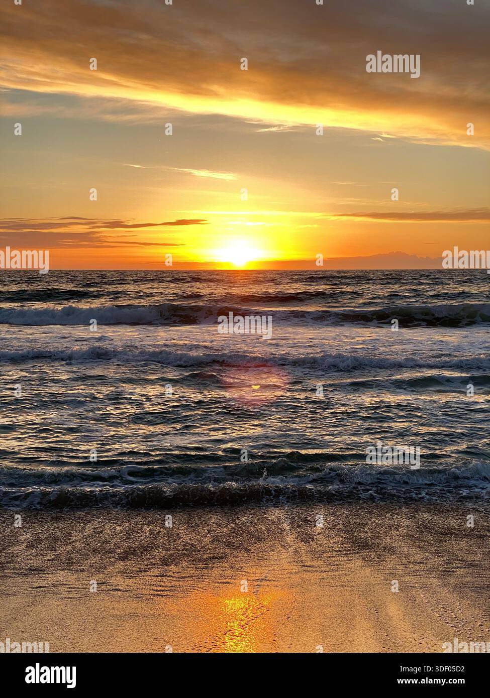 onde dell'oceano all'alba, con luce dorata che si riflette sull'acqua e nuvole colorate nel cielo - Immagine stock catturata con smartphone