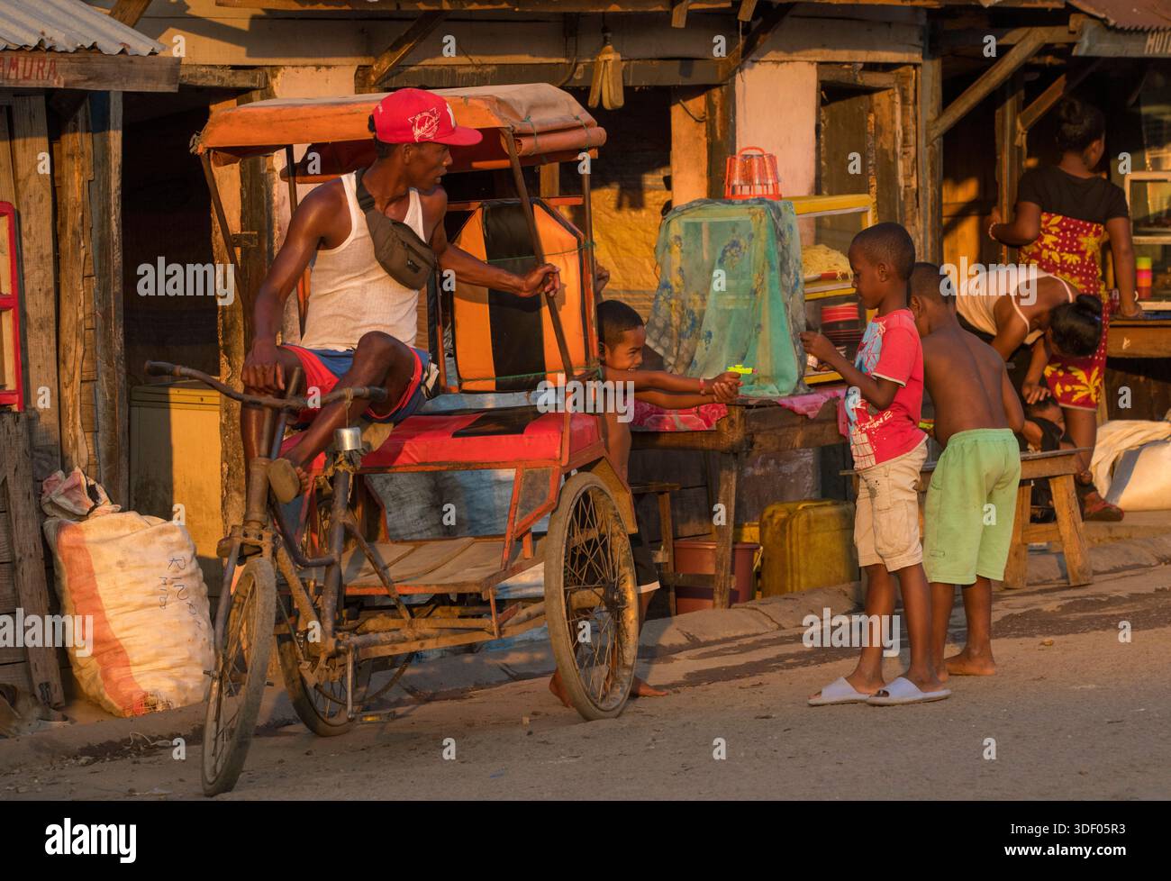 Ragazzi malgasci che hanno una battaglia con la pistola ad acqua alla luce del mattino presto, Miandrivazo, Madagascar. A Miandrivazo, i risciò in bicicletta sono comuni e rappresentano un'opzione di trasporto conveniente e conveniente. Foto Stock
