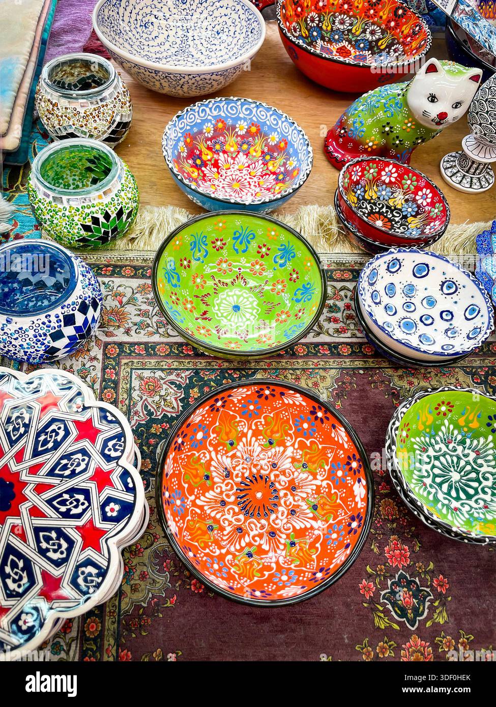 Mostra colorata di ciotole in ceramica finemente dipinte, lampade a mosaico e una statuetta decorativa di gatto su un tappeto di mercato a motivi geometrici Foto Stock