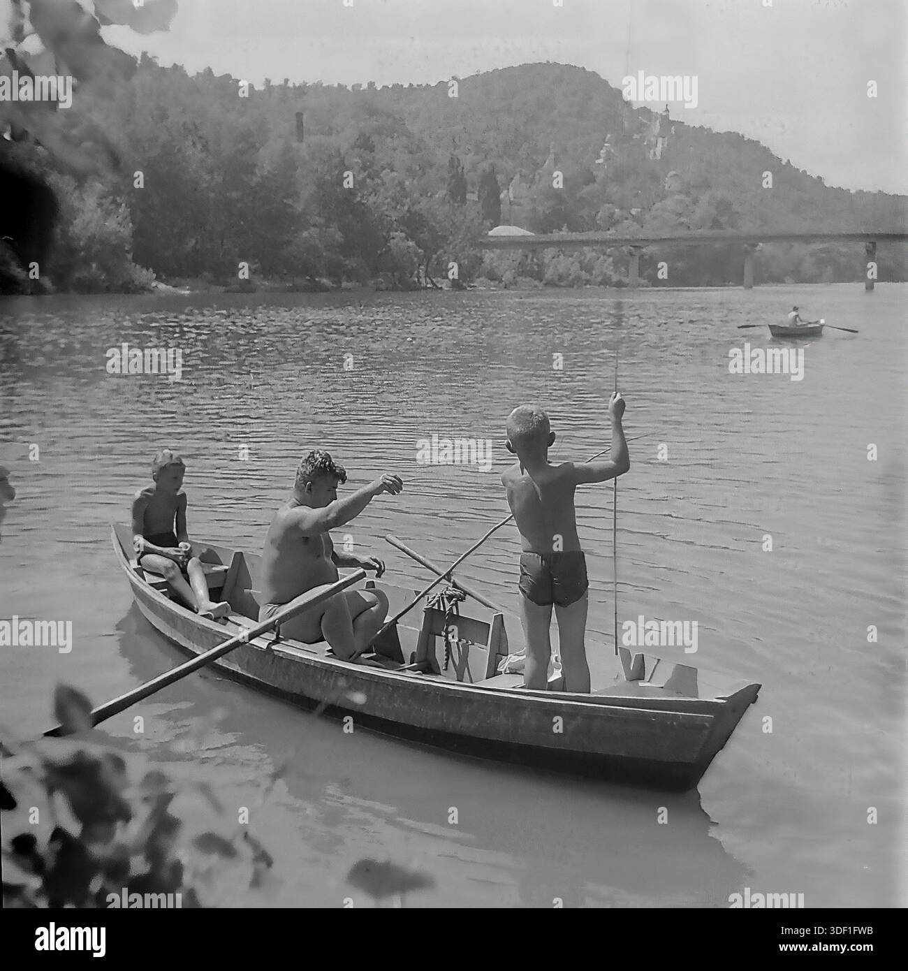Sviatohirsk, regione di Donetsk, Ucraina, URSS. 1970 anni Una gita di pesca in famiglia su una barca di legno sul fiume Seversky Donets. Un uomo adulto e due ragazzi si rilassano sull'acqua in una soleggiata giornata estiva. Un ragazzo è in piedi con una canna da pesca. Sullo sfondo, c'è un paesaggio pittoresco con montagne di gesso, una fitta foresta e un ponte di cemento sul fiume. Sulla collina sono visibili il monumento ad Artem e il complesso architettonico del monastero. Foto storica delle vacanze estive in Unione Sovietica. Atmosfera autentica di vita tranquilla, infanzia e attività ricreative all'aperto. Foto Stock
