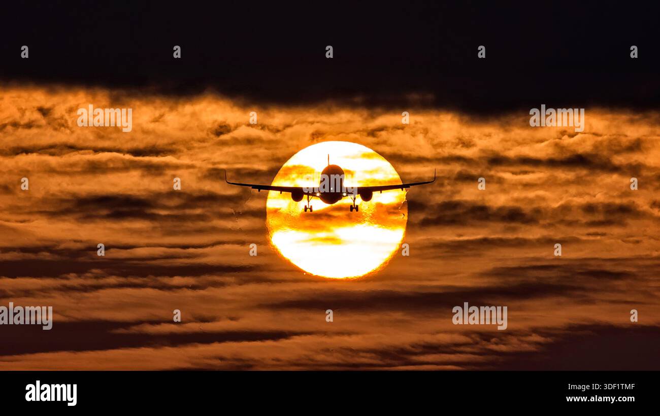 Vista di un aeroplano sagomato che sale contro un tramonto infuocato, le ali allungate, creando un contrasto sorprendente con il sole splendente, Schiphol Foto Stock