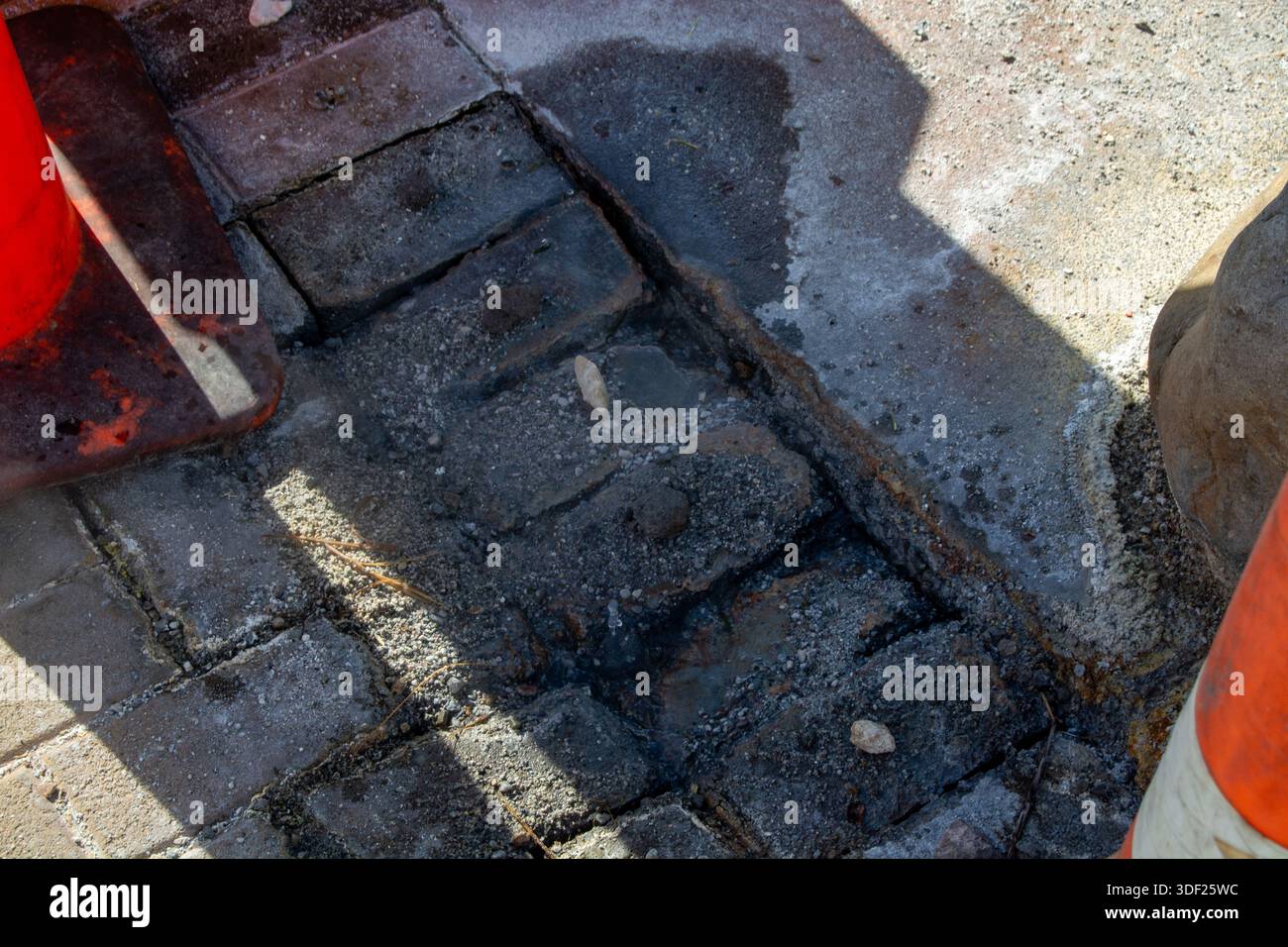 Vista ravvicinata di un cantiere che mostra pavimentazioni irregolari in mattoni con ghiaia e detriti. I coni stradali sono parzialmente visibili, a indicare la W in corso Foto Stock