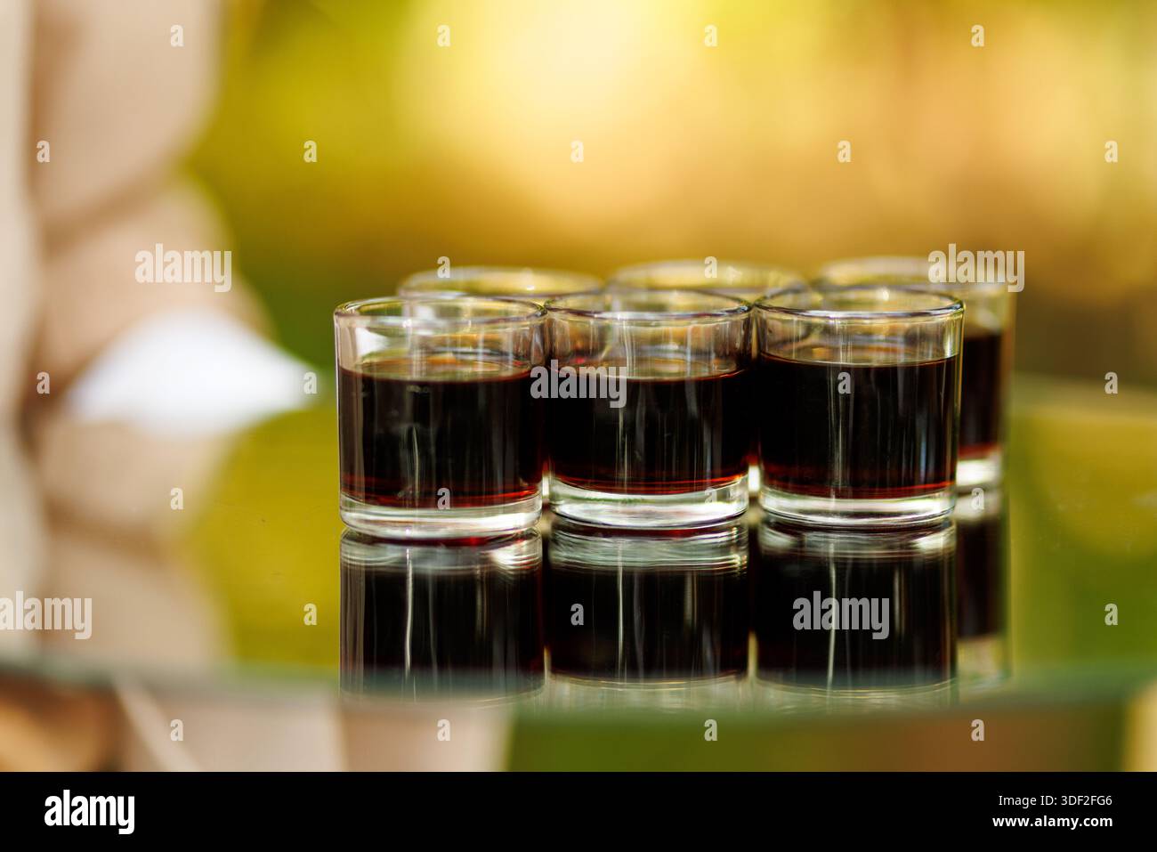 Diversi piccoli bicchieri riempiti di liquido scuro disposti in fila su una superficie riflettente. Foto Stock