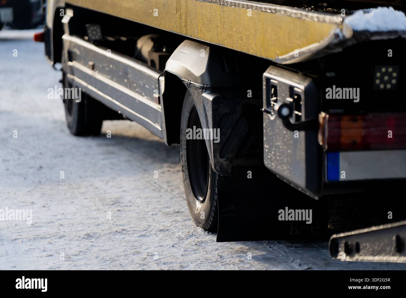Sezione posteriore del carro attrezzi con pianale che mostra la ruota del parafango e il vano portaoggetti laterale parcheggiato su un terreno innevato, evidenziando i dettagli del veicolo commerciale e il verricello Foto Stock