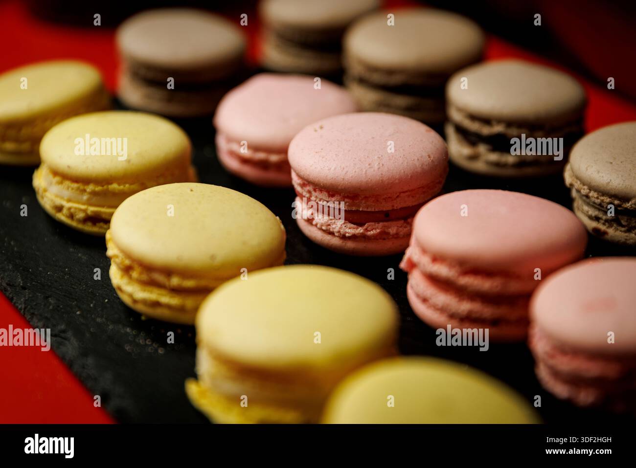 Selezione di macaron pastello disposti su un piatto di ardesia scura. Foto Stock