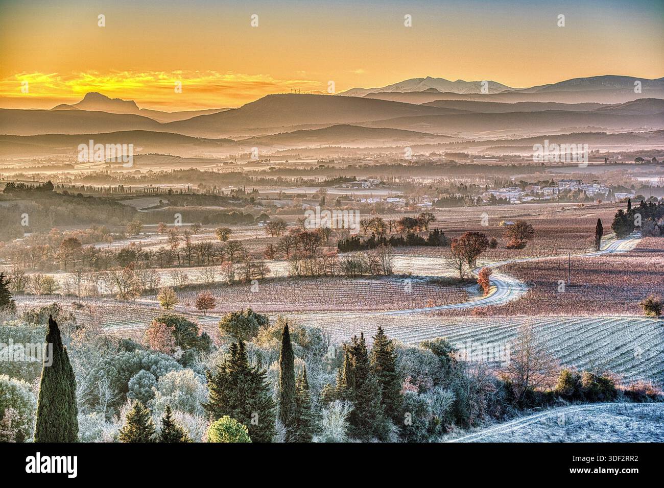 Un tranquillo paesaggio invernale con gelo che copre i campi ondulati. Il sole che sorge getta un caldo bagliore sulle montagne lontane. Foto Stock