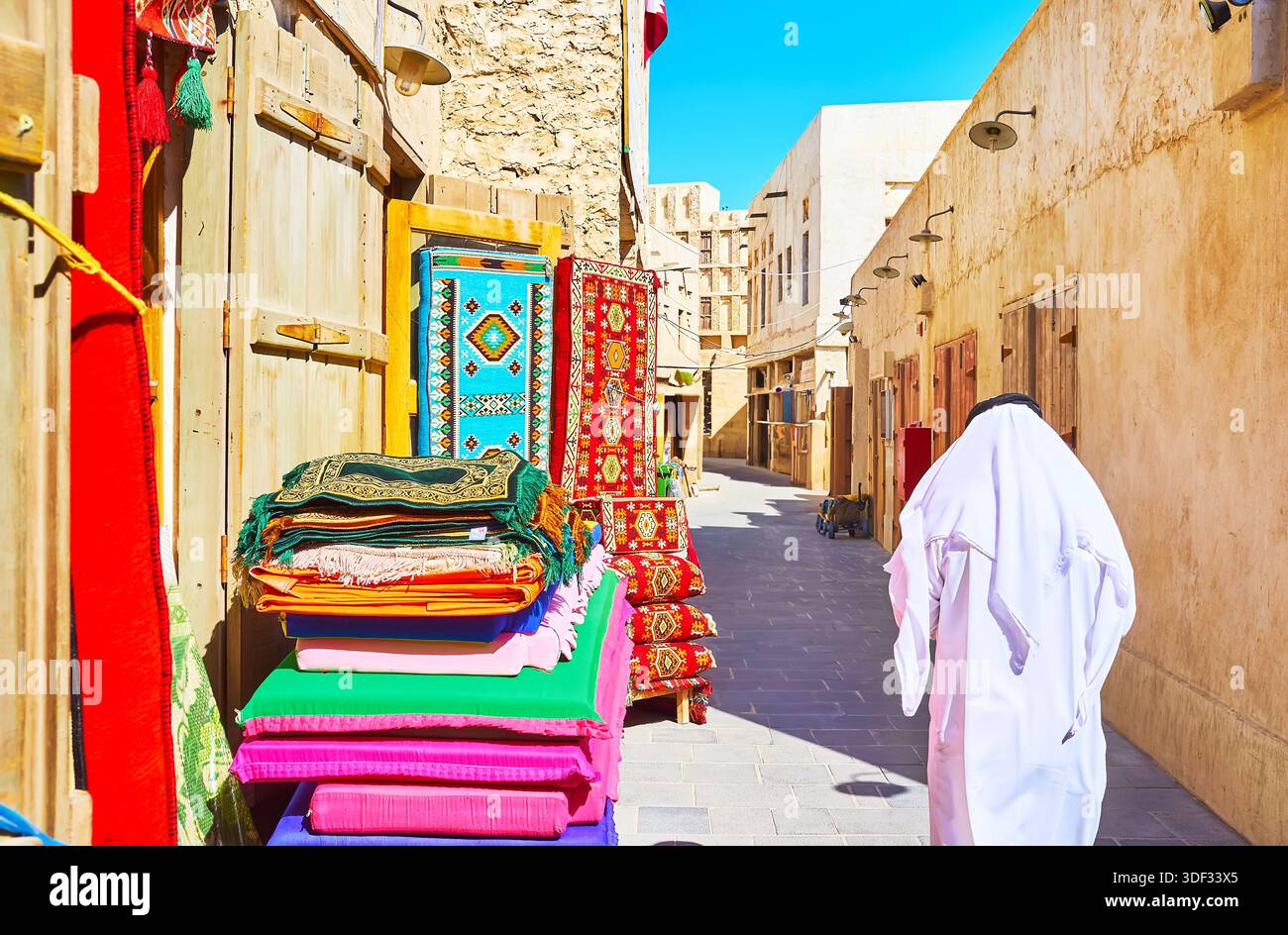 DOHA, Qatar - 13 febbraio 2018: il negozio di tappeti in strada stretta di Souq Waqif, la gente del posto a piedi lungo la strada in abito tradizionale - keffiyeh (headsc Foto Stock